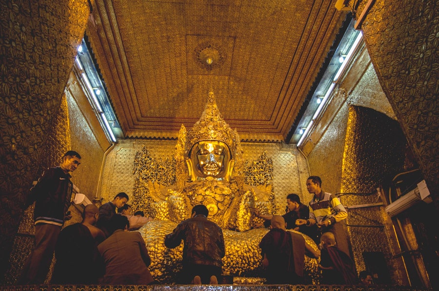 Worshippers applying gold leaf to a buddha at Mahamuni Paya in Mandalay , Myanmar