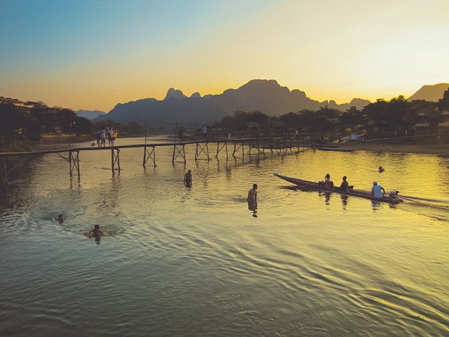 Laos travel photography: Scene in Vang Vieng with people swimming and boating in the Nam Song river