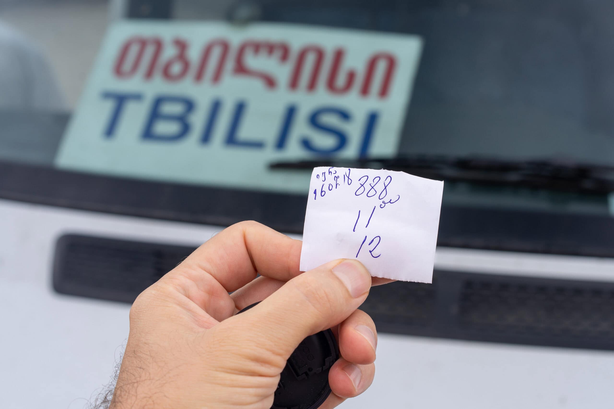 I'm holding a hand written minivan ticket for the Sighnaghi-Tbilisi route. You can see Tbilisi written in English and Georgian displayed in the van's window behind the ticket