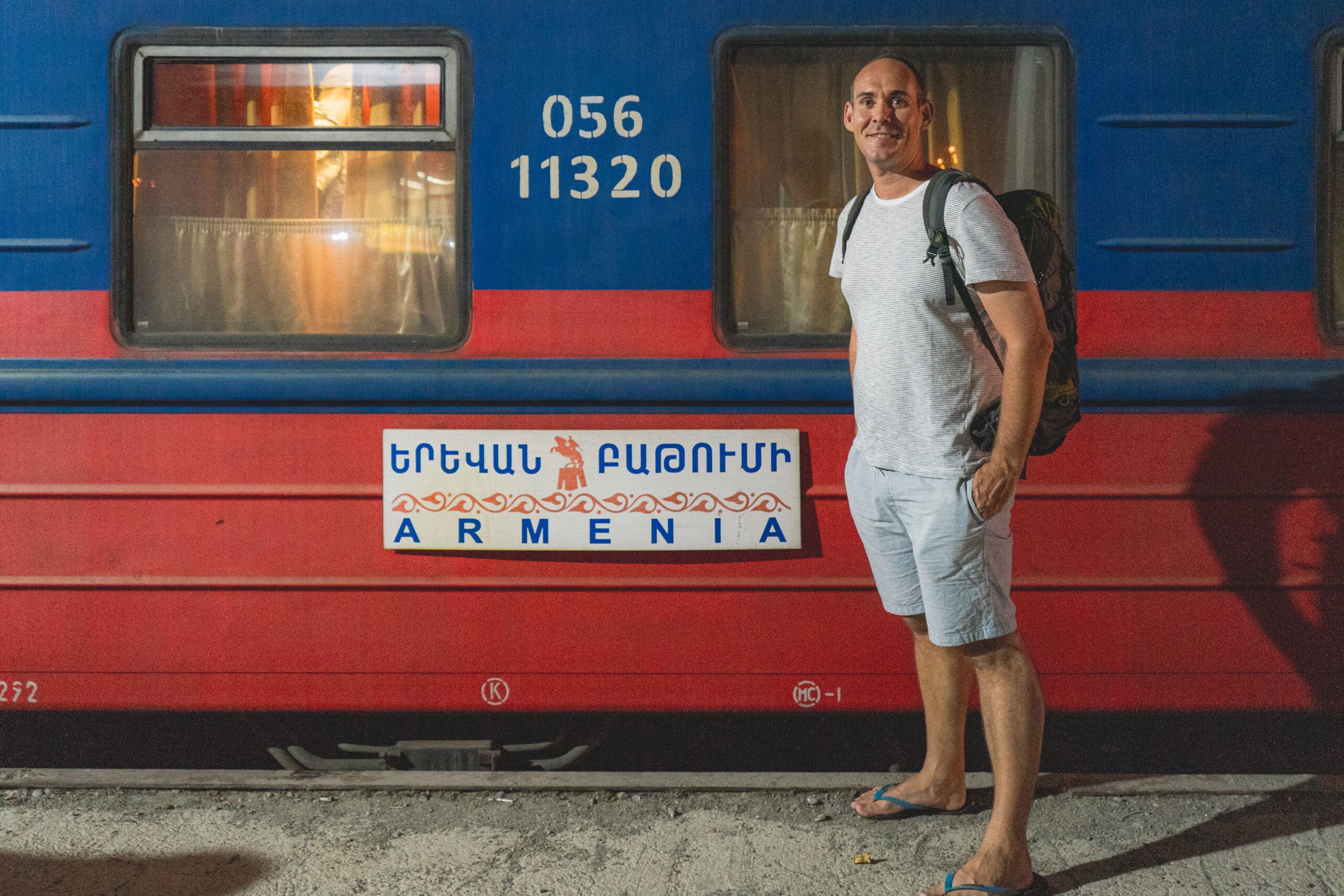 I am standing with my backpack in front of the red and blue Armenia night train