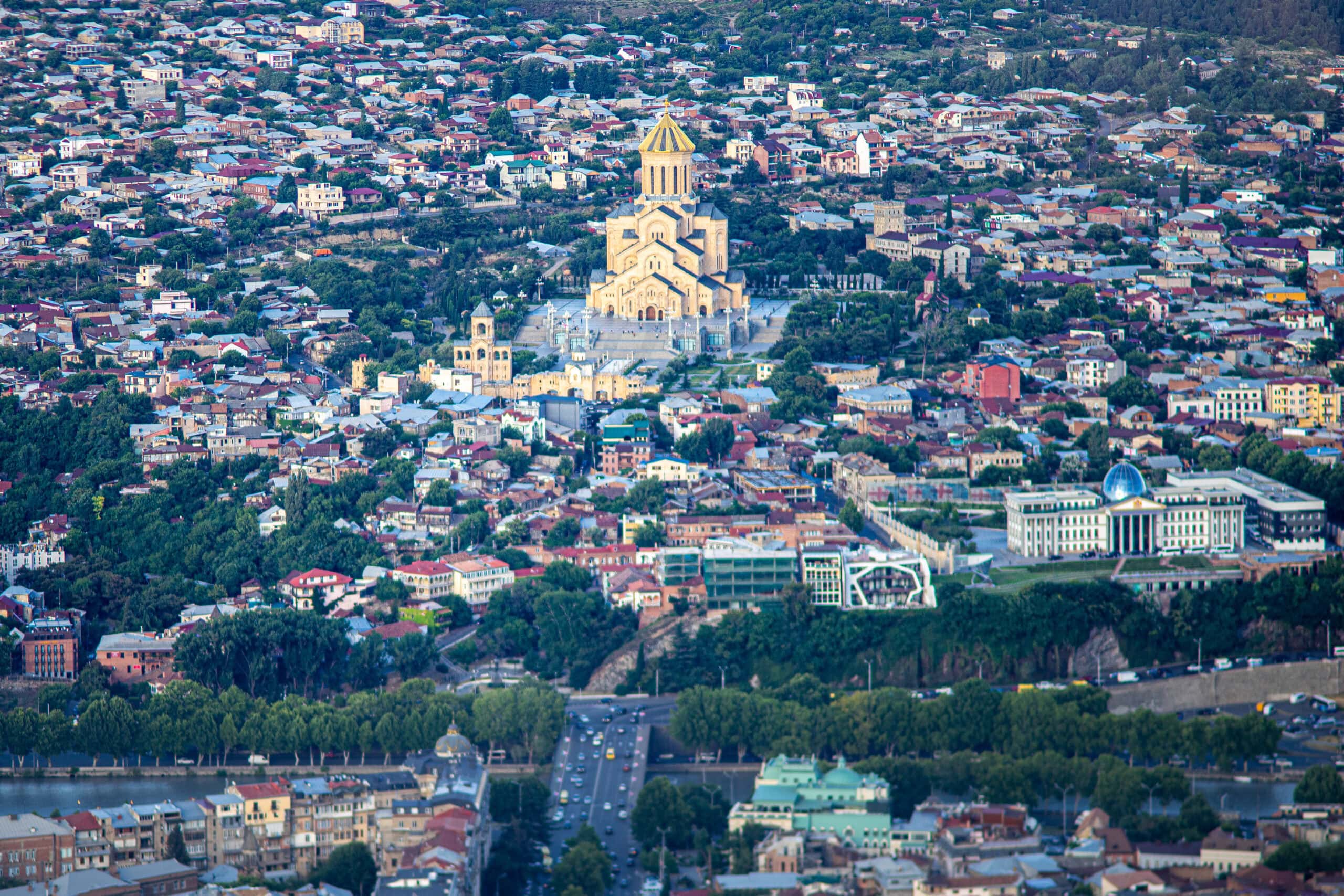 A huge, golden brown cathedral surrounded by small houses and trees seen from Mtatsminda Park in Tbilisi Georgia