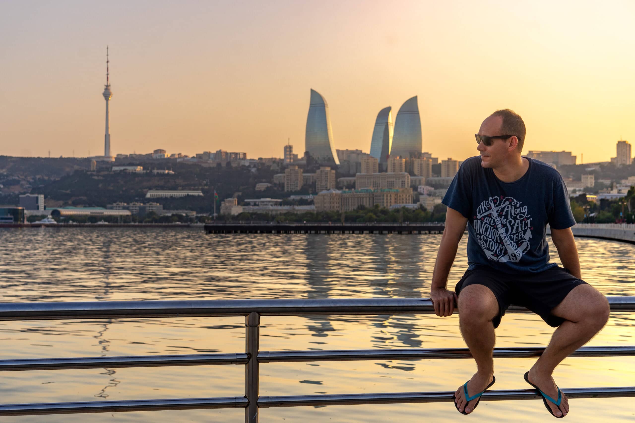 I'm sitting on a railing with the Caspian sea and the Baku Flame Towers behind me, during sunset
