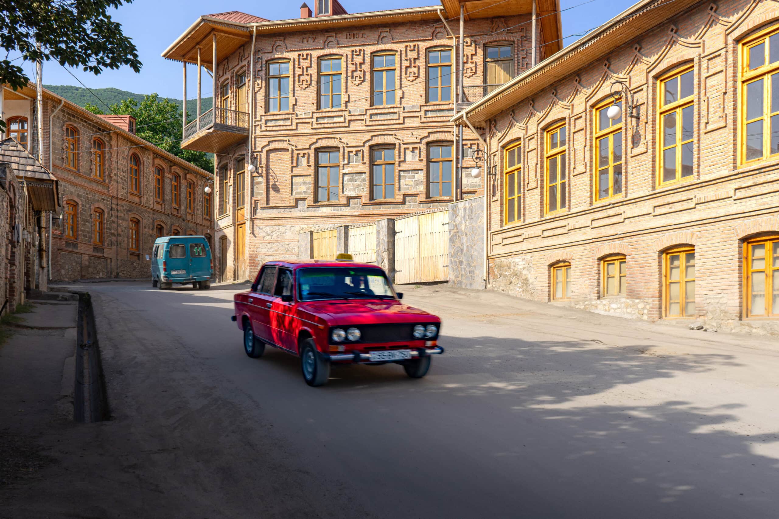 A red Lada drives past a beautiful brick building in Sheki, Azerbaijan