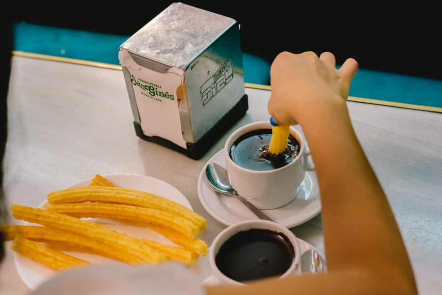 Jin dips a churro into hot chocolate in Madrid