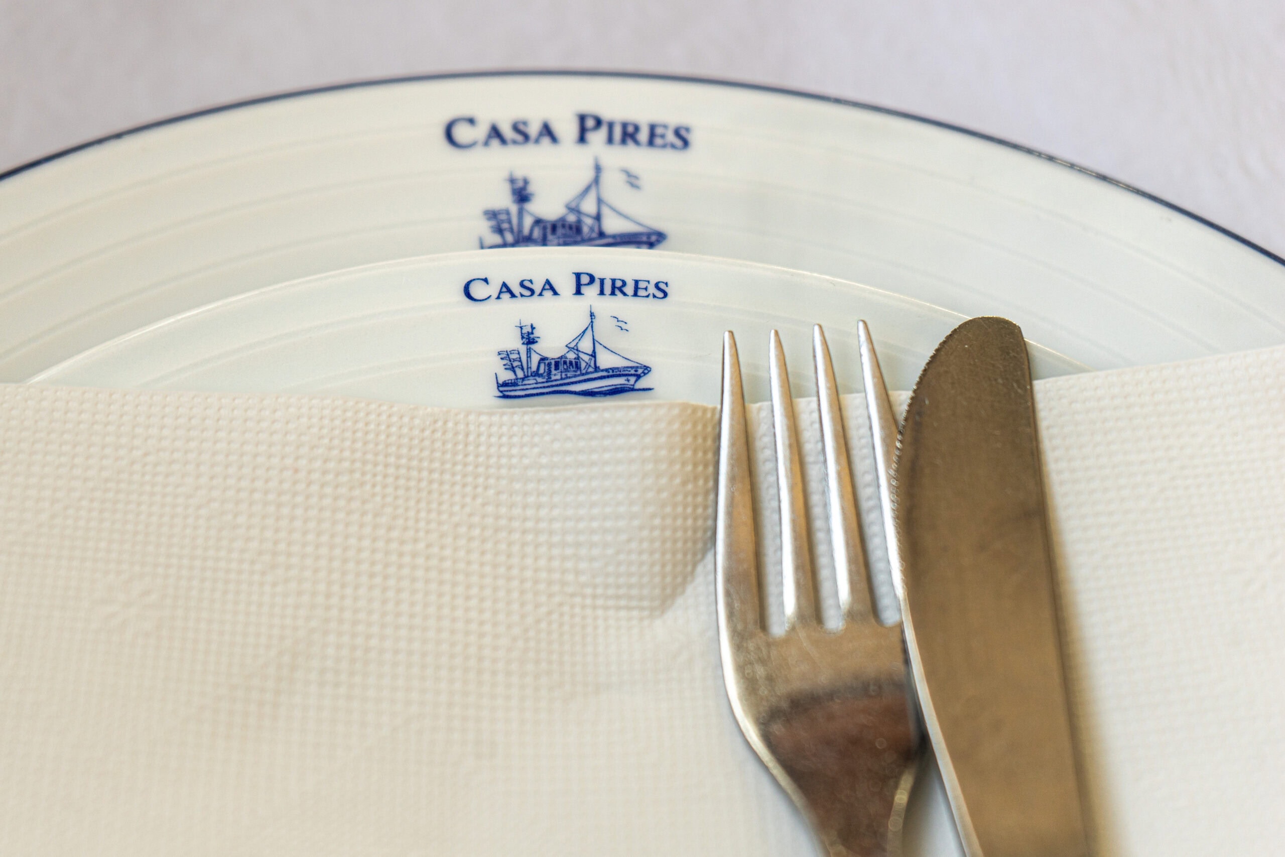  Plates with the Casa Pires logo. A knife and fork are resting on a napkin on the plates. It's a great seafood restaurant in Nazare, Portugal
