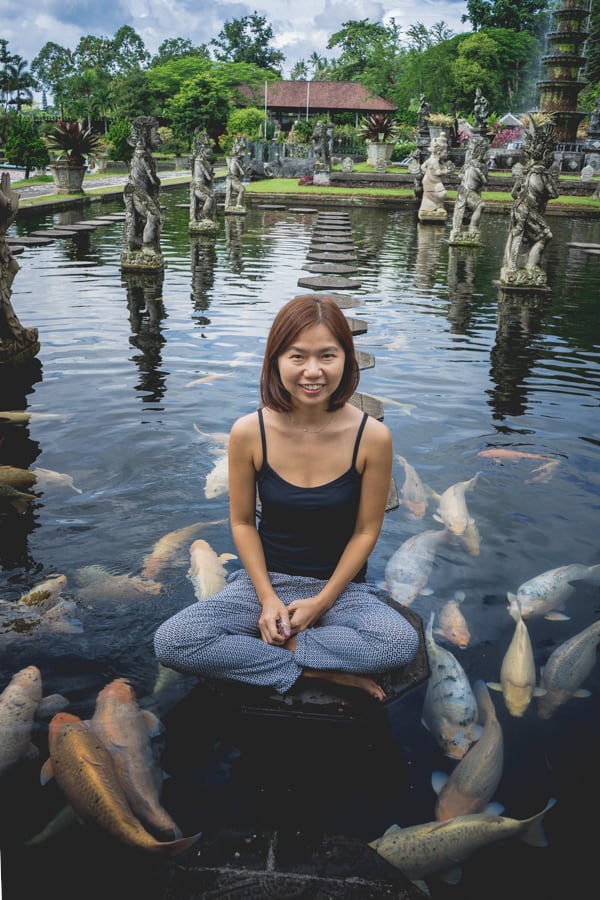 Jin posing on a stepping stone in a pond at Tirta Gangga with giant koi fish swimming around her