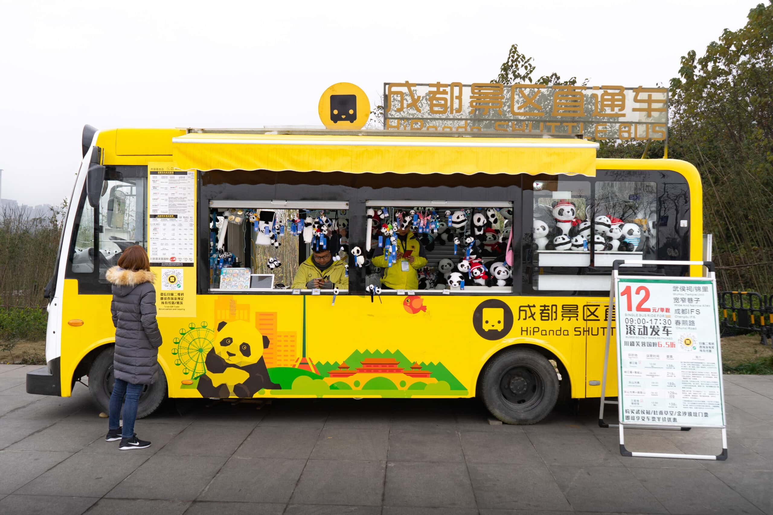 The yellow HiPanda Shuttle bus that runs between the Panda Base and Chengdu City. Jin is reading the time table and routes displayed on the side of the bus