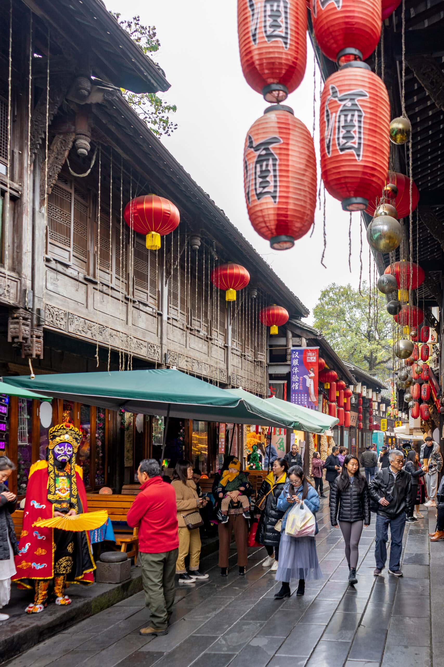 Shoppers walk down Jinli Street. There is a Sichuan face changer who tries to attract visitors standing outside a shop