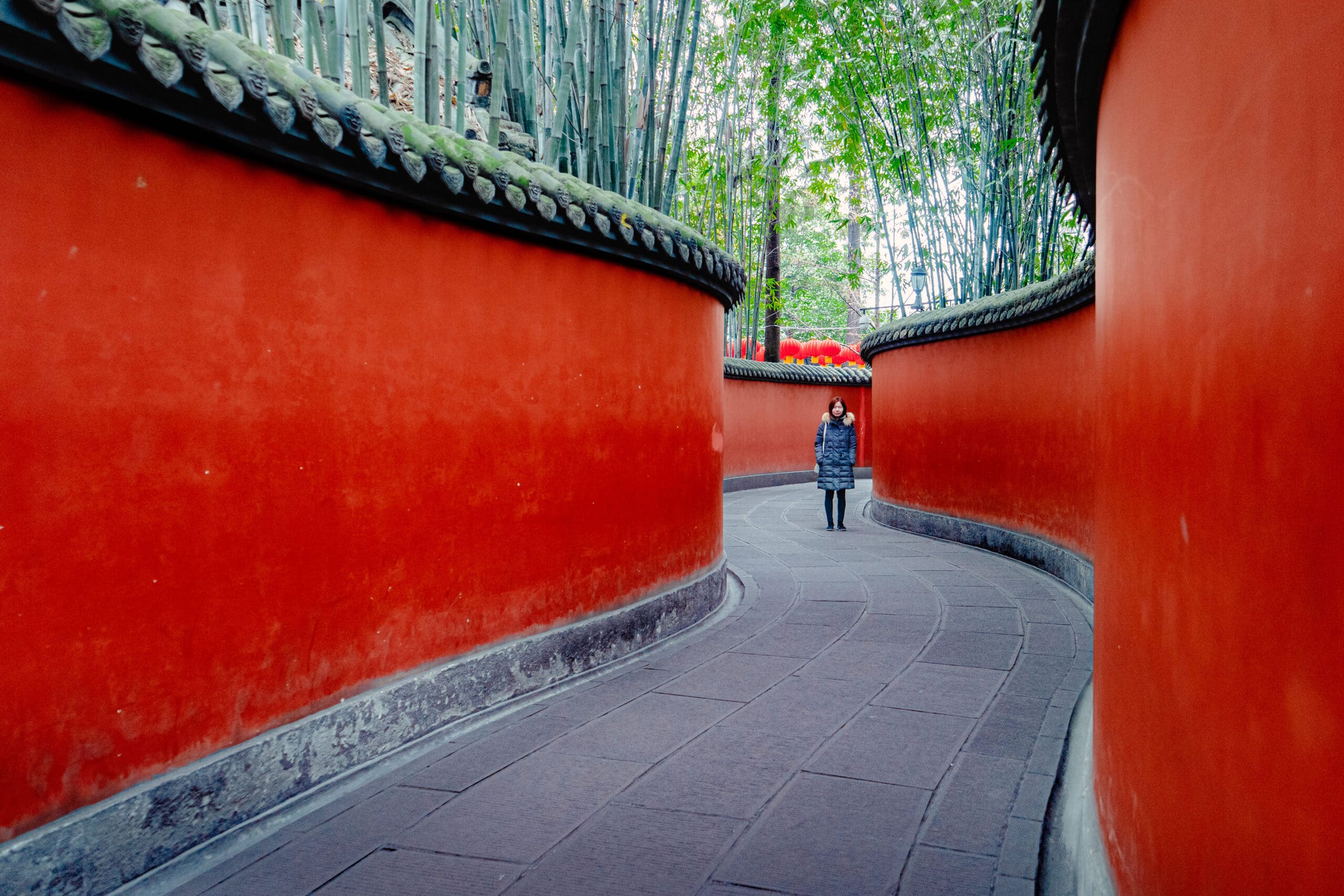 Jin stands between two curving, red walls of the Wuhou temple in Chengdu