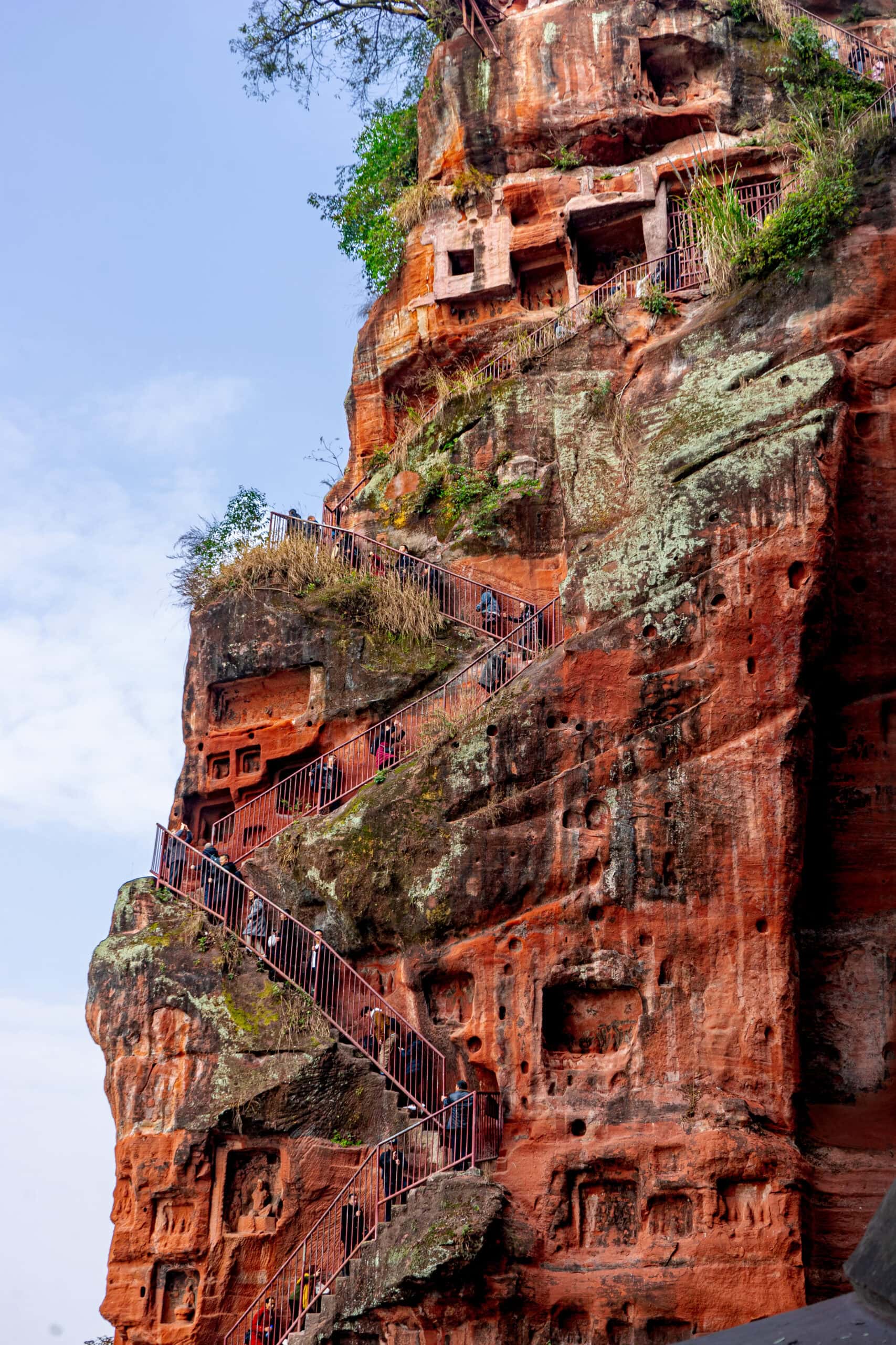 Stairs zig zag up a red cliff to the top of the Leshan Buddha