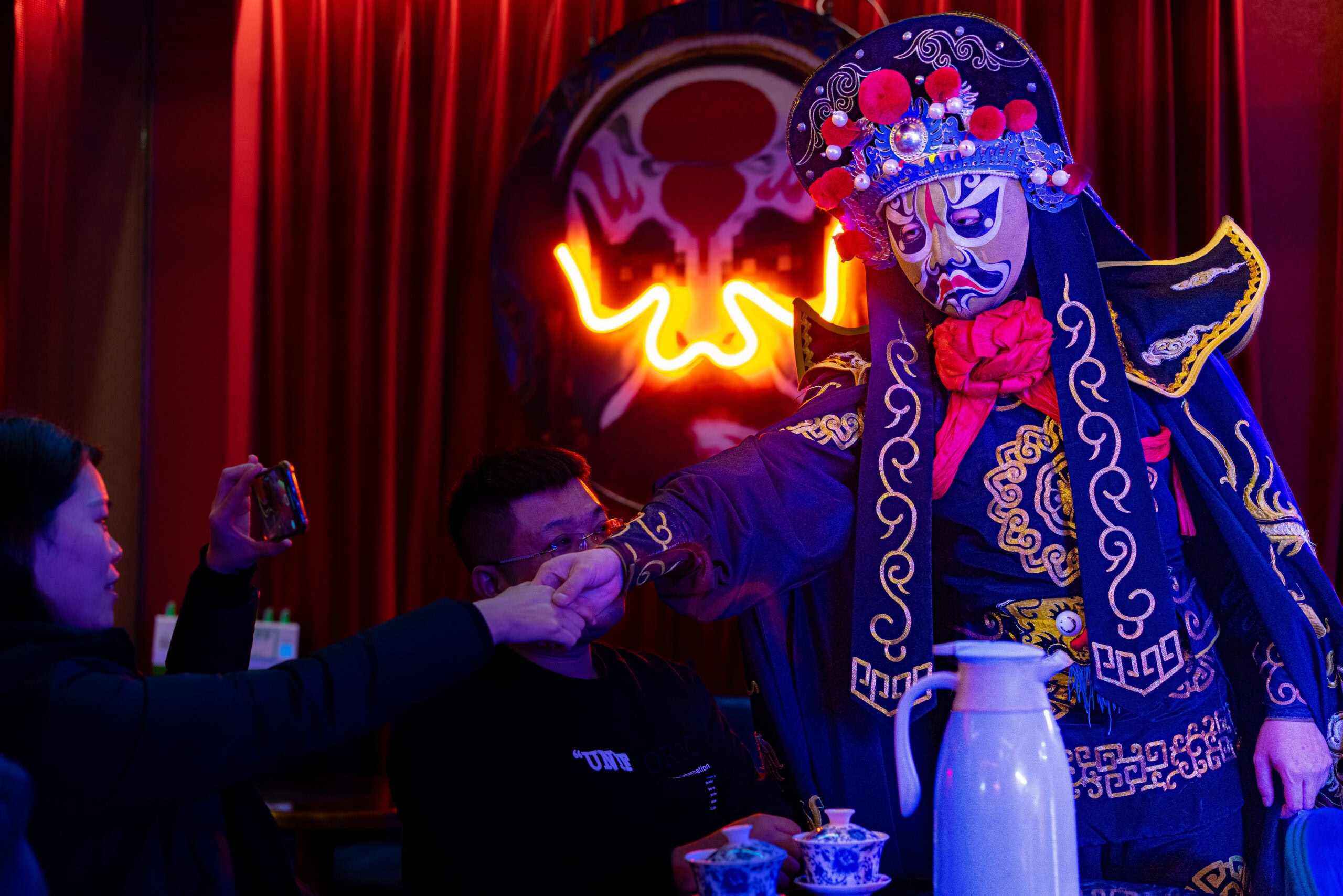Chinese face mask changing show in Chengdu. Ther performer is going from table to table and do a face change right in ftont of you. Here the performer is shaking hands with an audience member, who is taking a video of the entire thing on her smart phone
