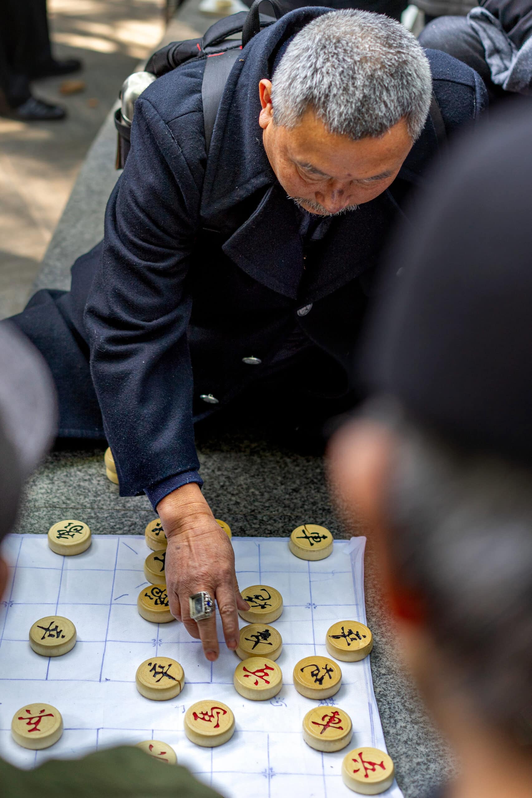 An elderly man wearing a huge, square ring on his middle finger makes a move in a Chinese chess game