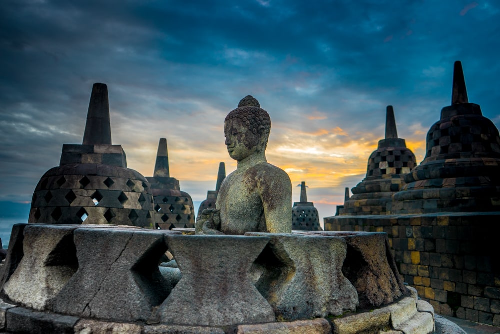 A buddha statue surrounded by stupas as sunrise on the upper tier of Borobudur temple in Indonesia