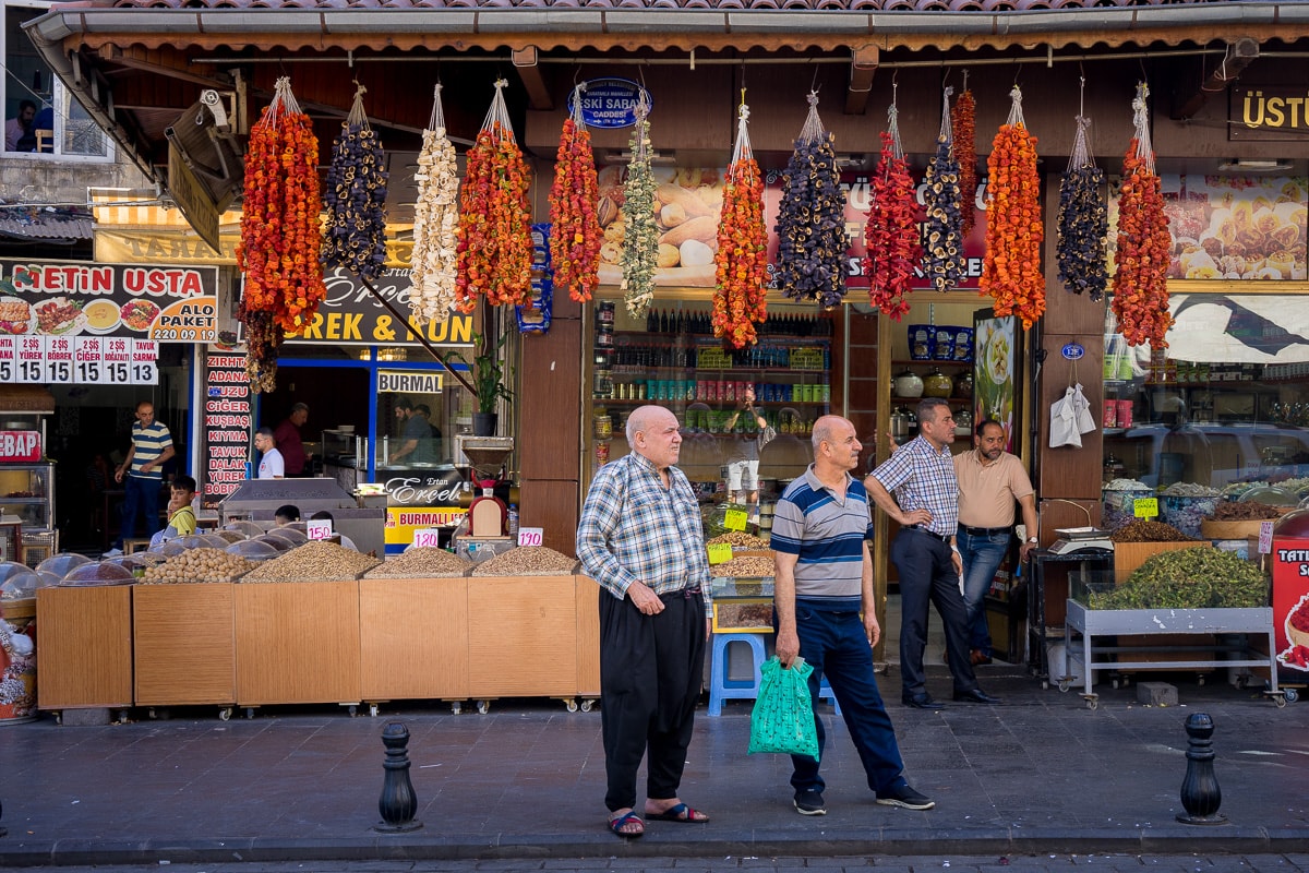 Men standing on street with dried vegetables and pistachio nuts for sale behind them