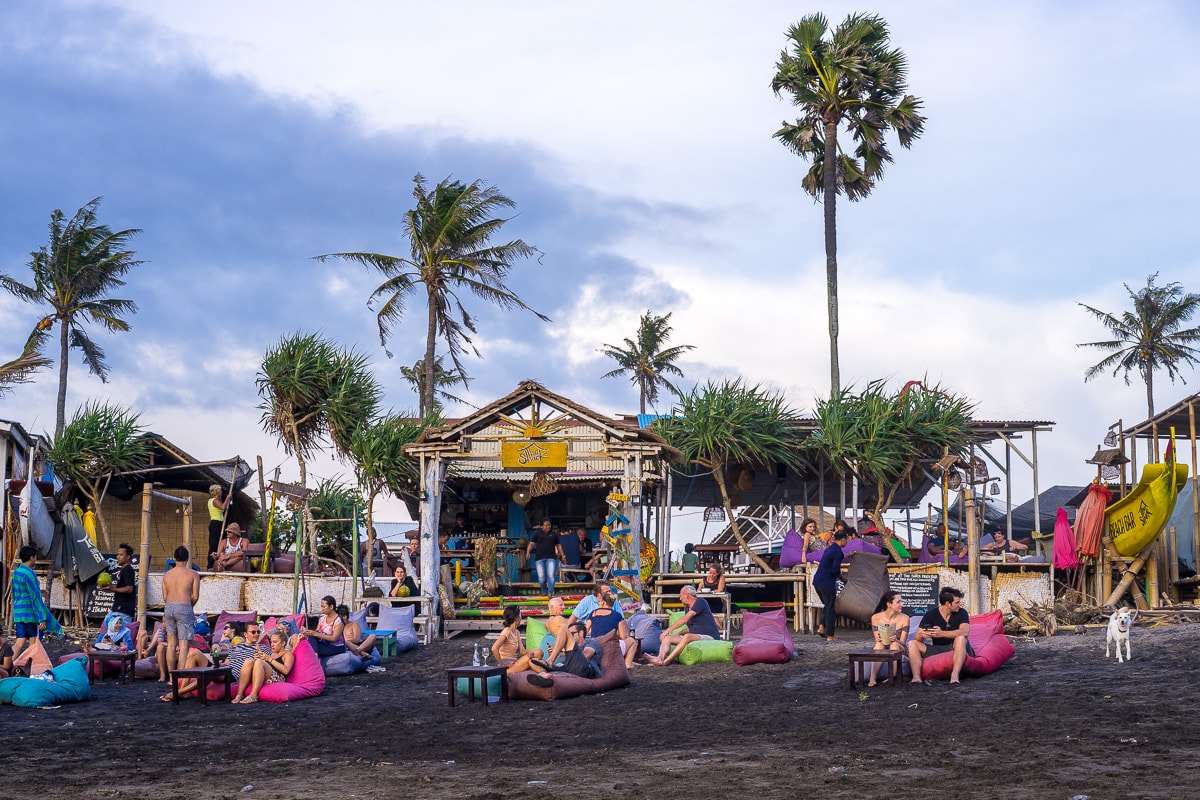 Holiday goers sitting on colourful bean bags enjoying sunset drinks at a beach bar in Canggu