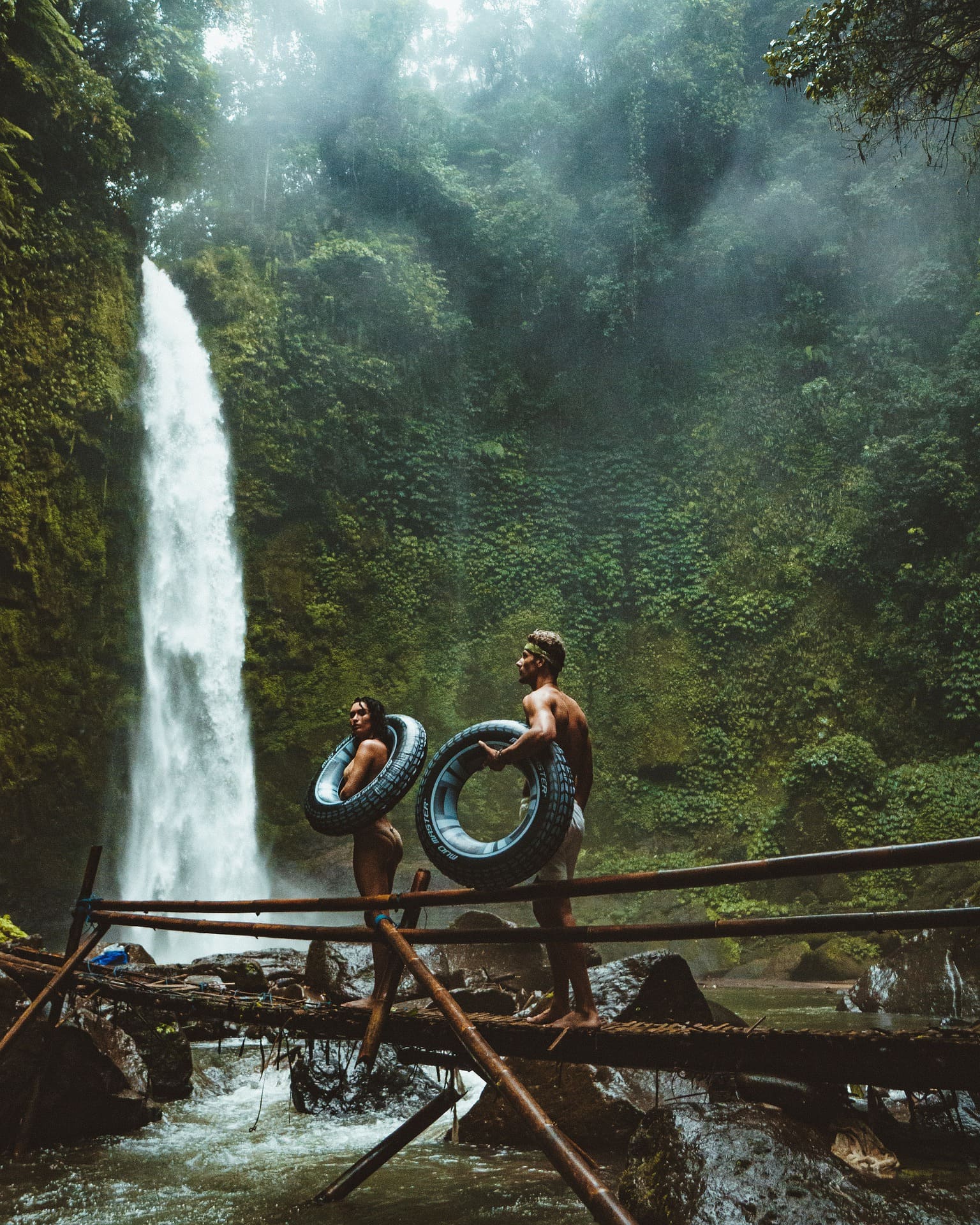 A man and a woman with inner tubes in front of a waterfall in Bali