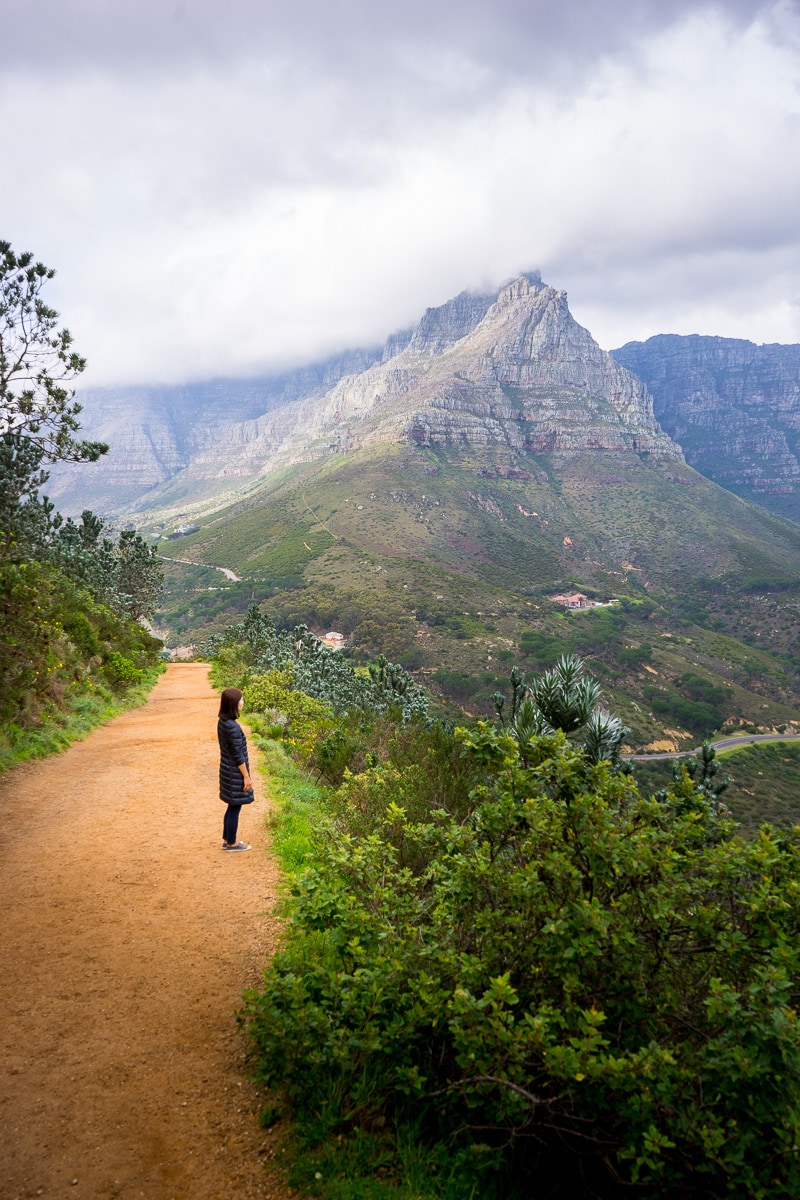  A woman hiking Lions Head with Table Mountain covered by clouds in the background
