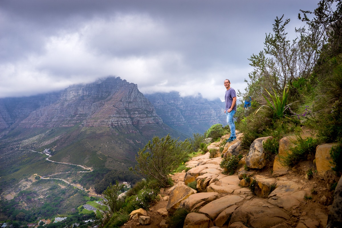 A man hiking on Lion's Head with Table Mountain covered in clouds in the background