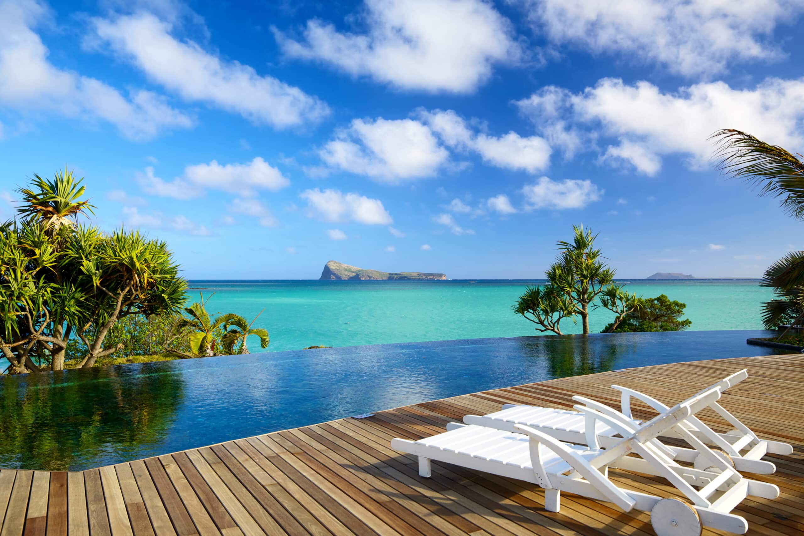 White sun chairs stand on a wooden deck next to an infinity pool overlooking the Indian Ocean in Mauritius