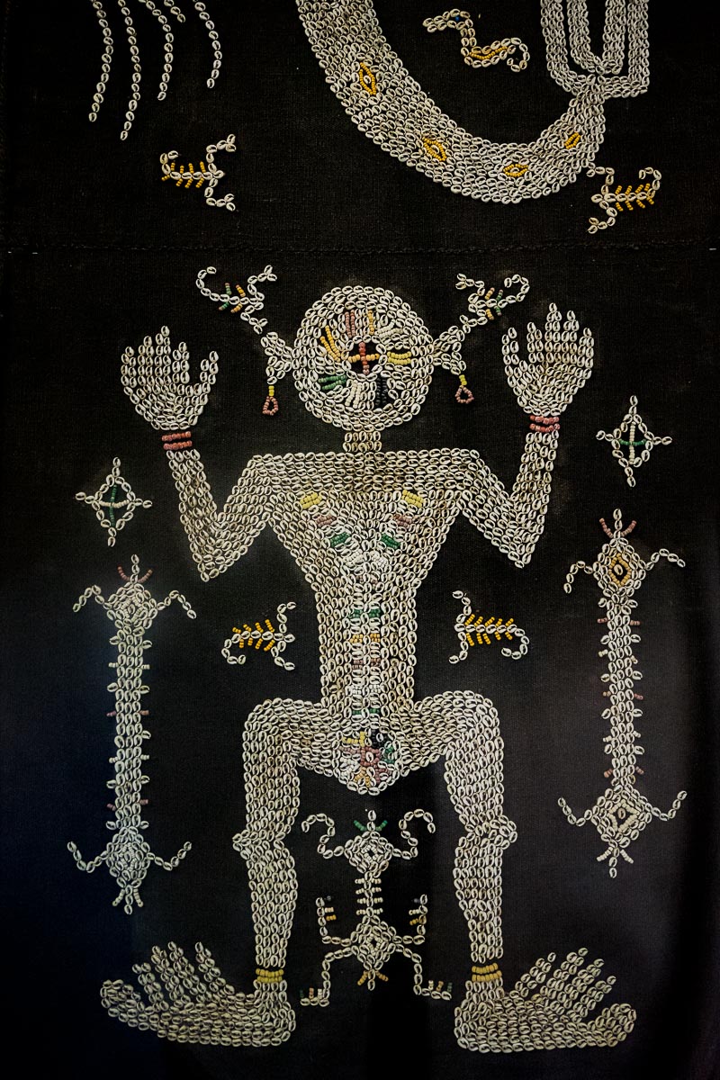 A beautiful Lau Hada sarong from Sumba island on display in the National Museum of Indonesia. It is made with white sea shells and colourful glass beads stitched on black cotton cloth to depict a primitive figure of a person.