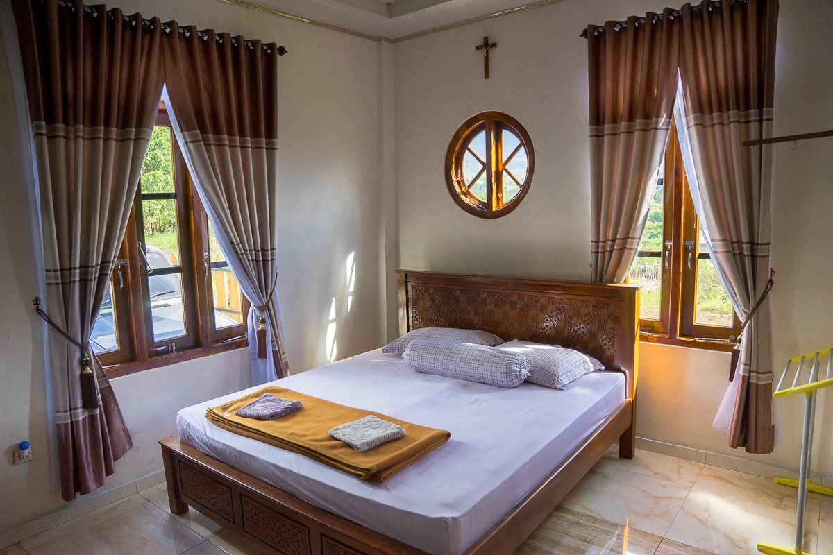 Our comfy room at Kopa Hilltop. There is a double bed, two large windows and a small round window above the bed.
