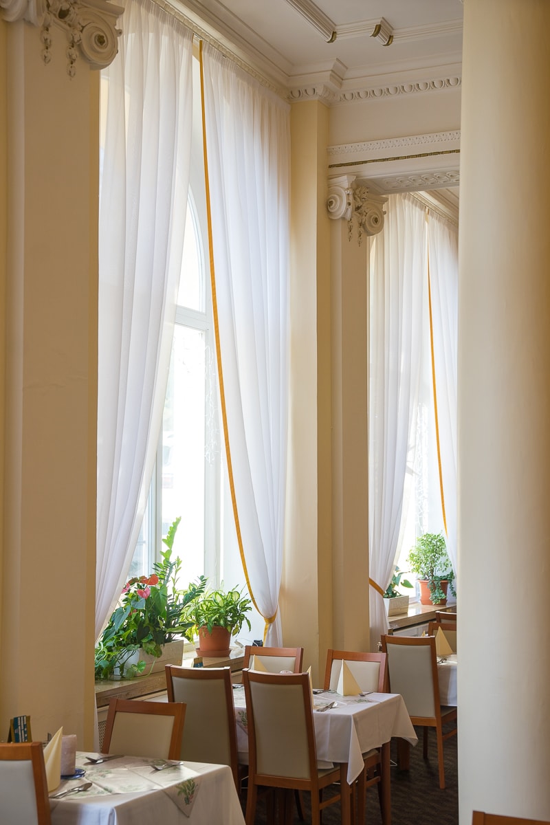 Dining tables and chairs between columns and live plants in the windows, seen in the dining room of the Spa hotel svoboda marianske lazne in the czech republic