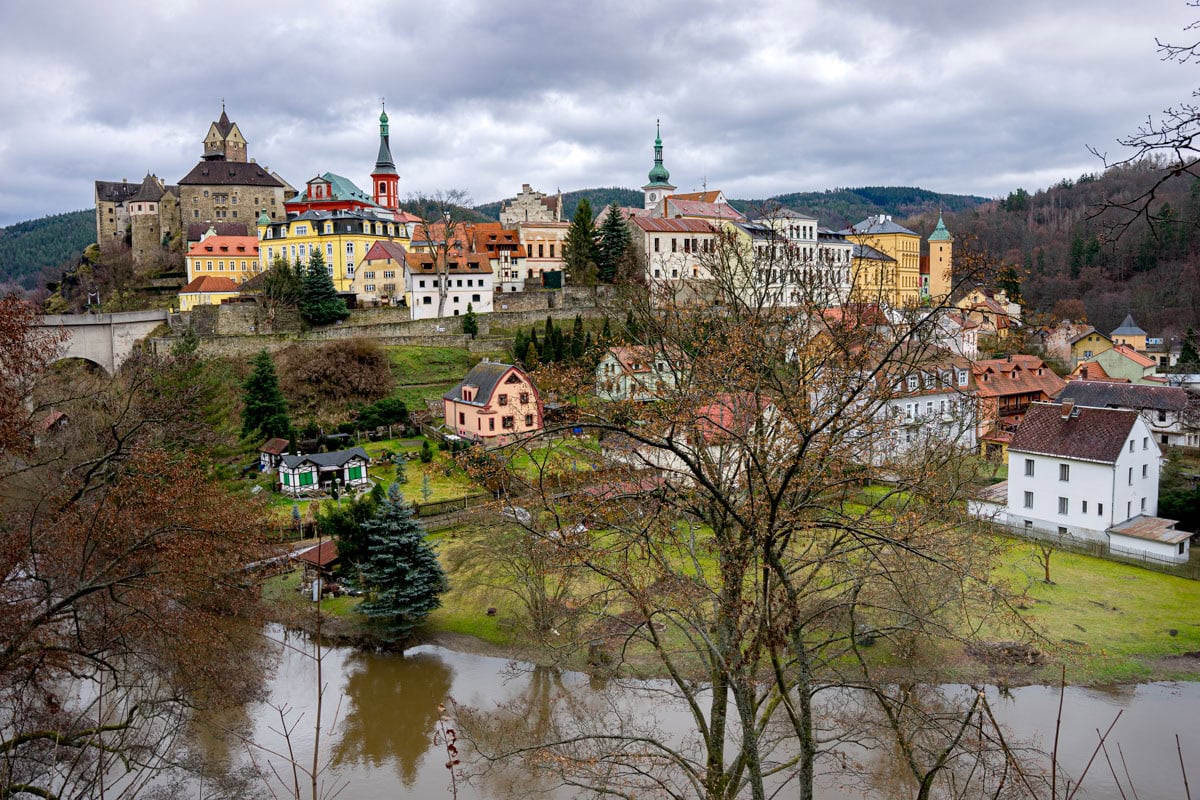A view of Loket towards the castle. In the foreground you can see pastel coloured houses on the bank of the Ohre River