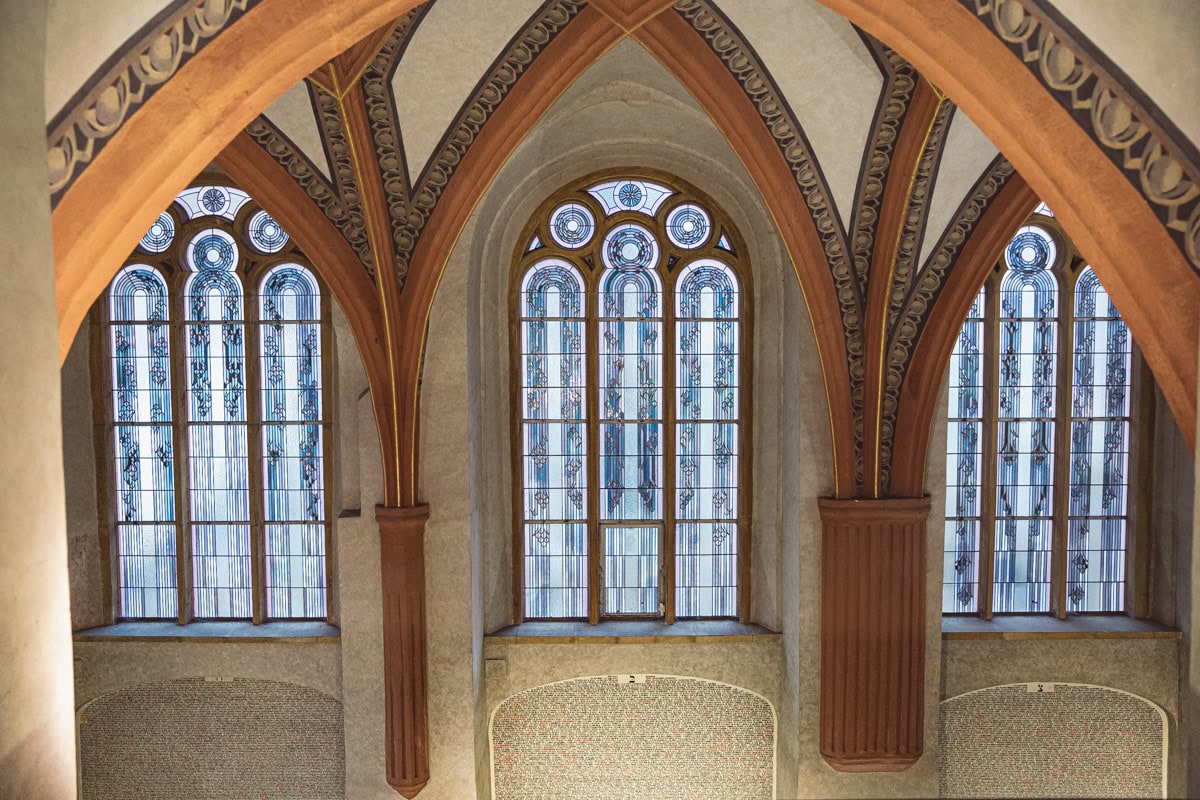 Arched windows with stained glass above the walls inscribed with the names of Holocaust victims inside the Pinkas Synagogue, Prague