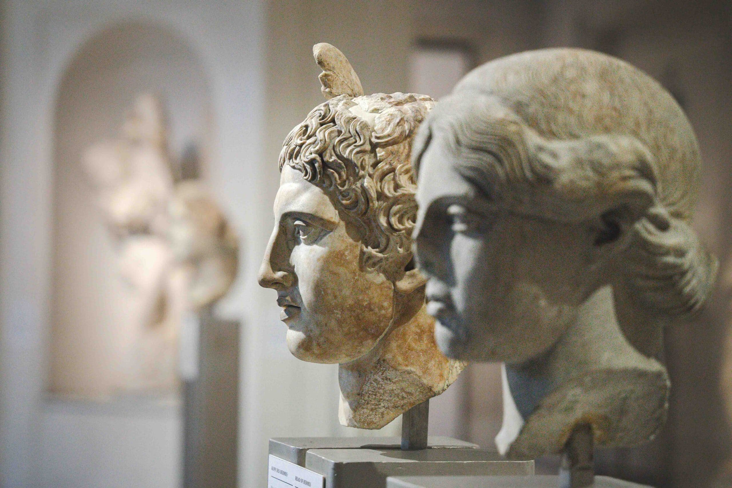 A close up of two marble heads in the Ephesus Museum in Vienna. The male head is that of Hermes (identified by the wing on his head and curly hair), and the woman's head is that of an unnamed goddess