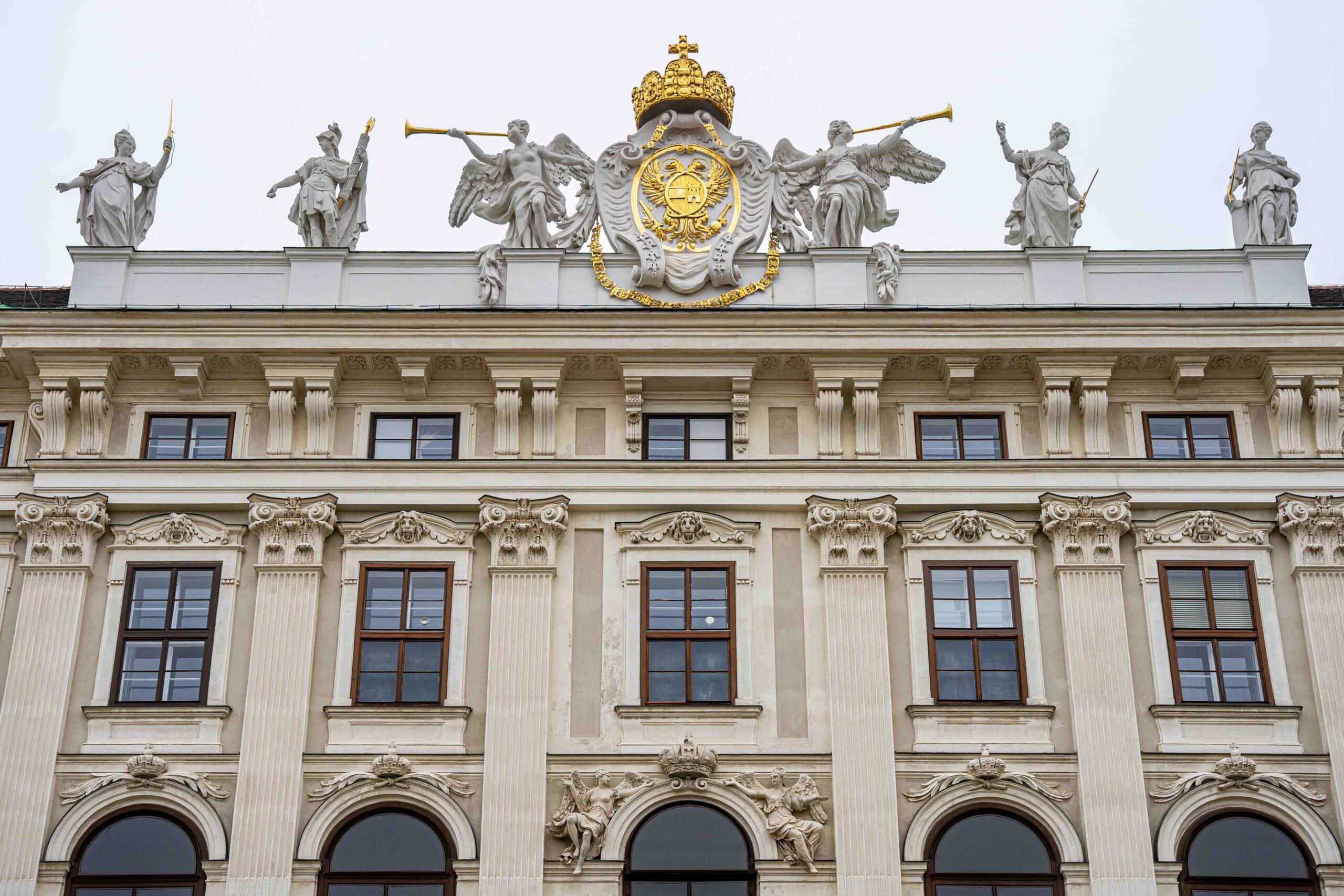 A detail of white statues and a golden emblem of double-headed eagles seen on a building in the Hofburg, Vienna