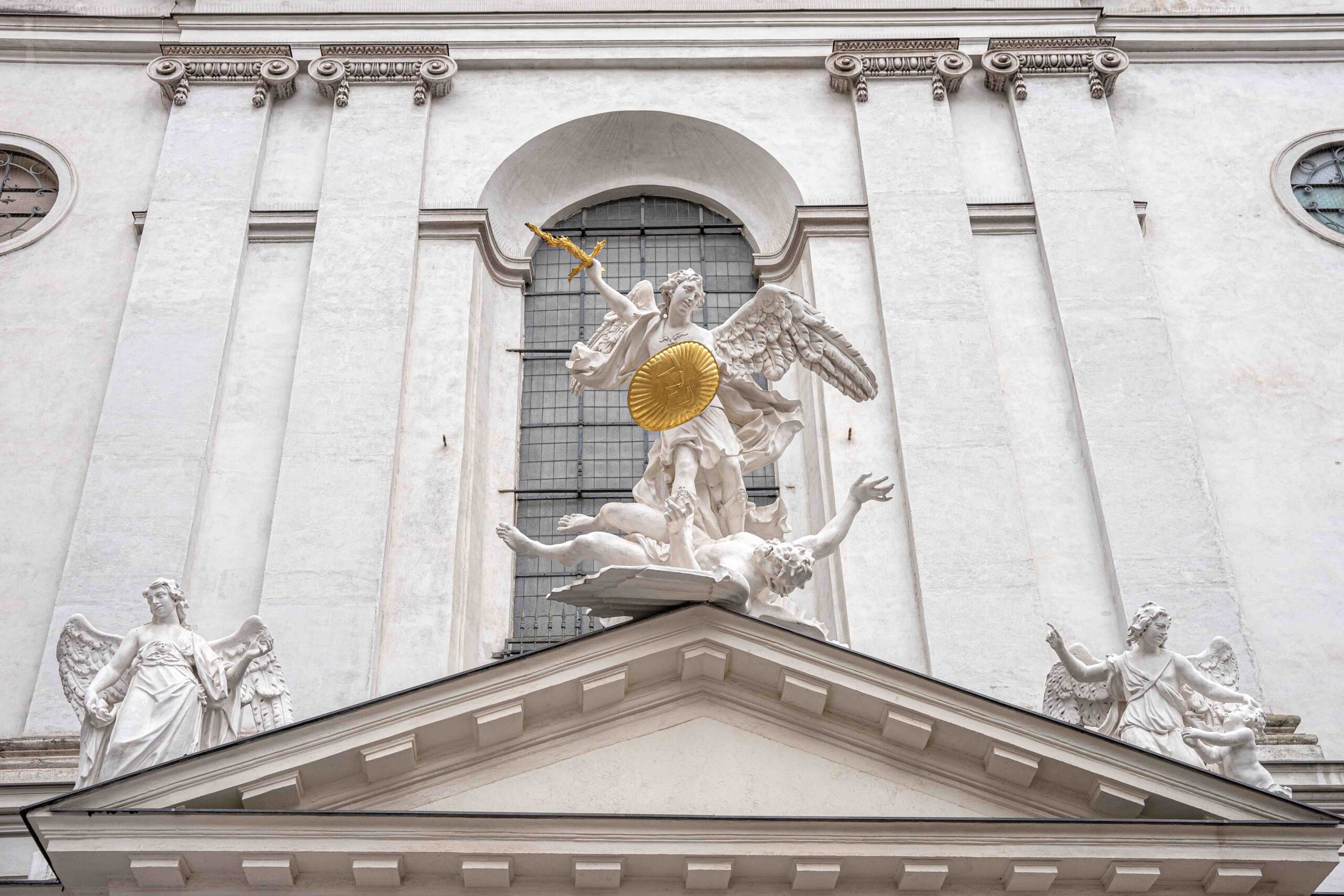 White statues standing on the frieze of a white Pfarre St. Michael (St Michael's Church) in Vienna