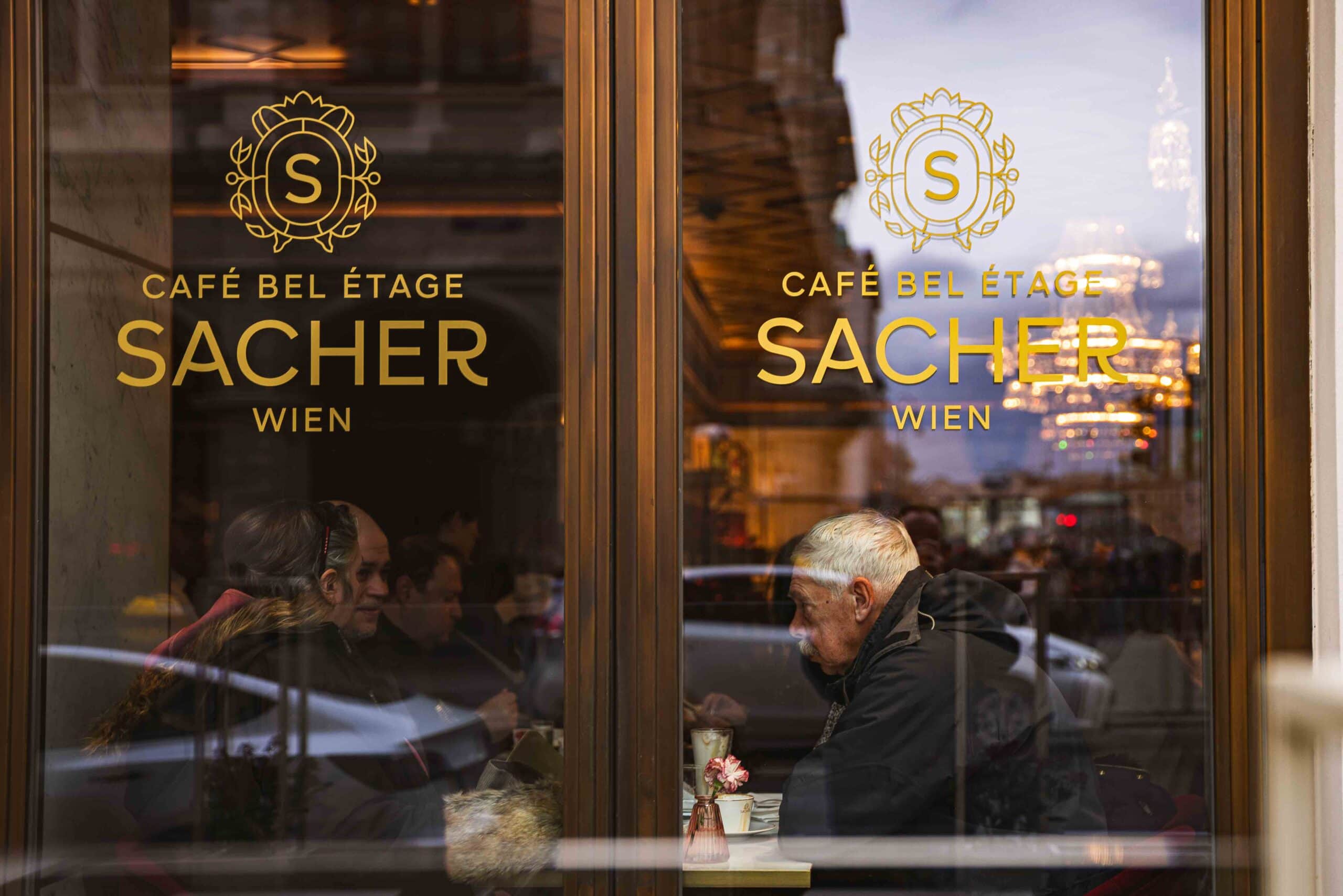 Customers seen through the window, sitting a a table at Cafe Sacher Wien