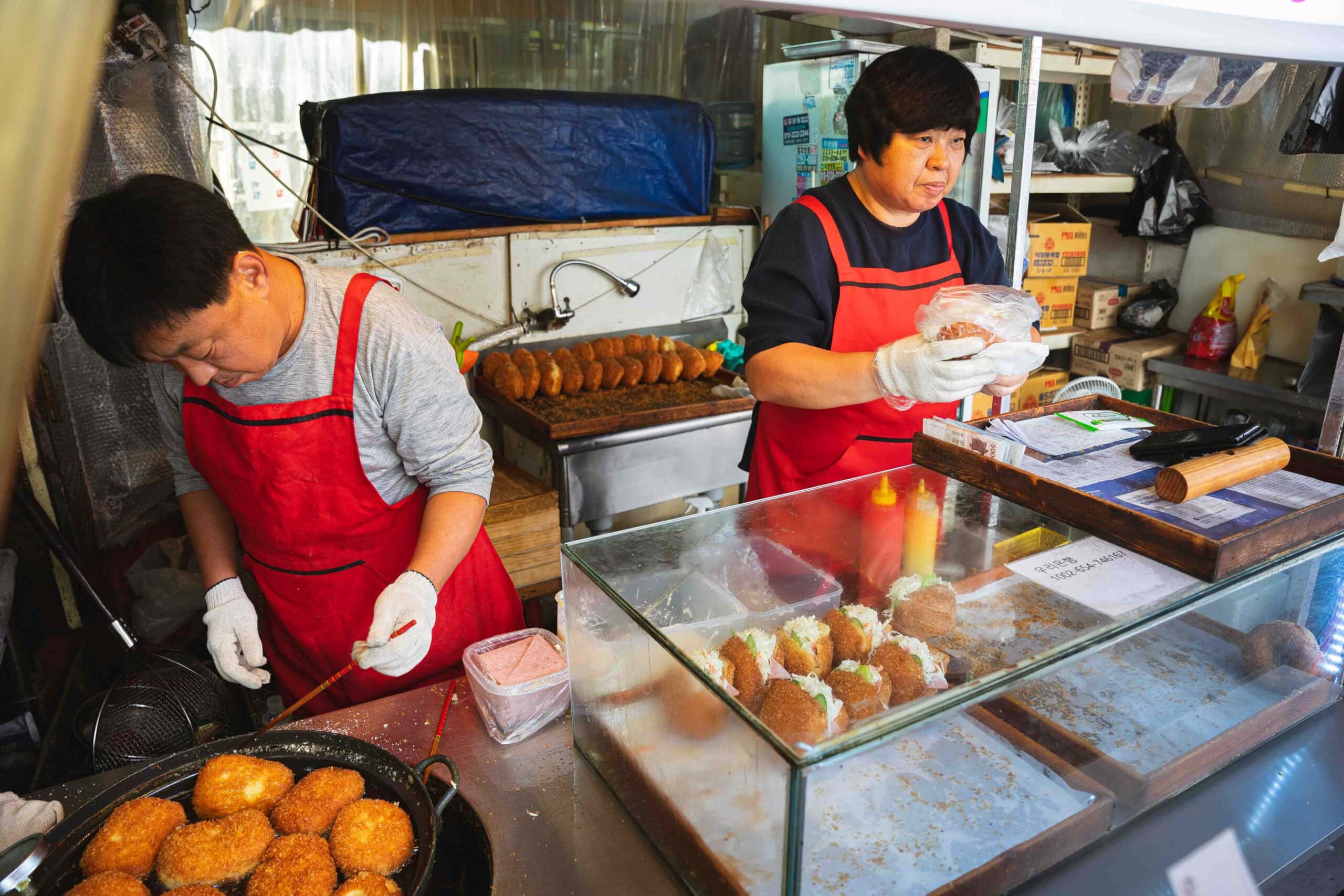 A couple wearing read aprons are selling croquettes filled with coleslaw and ham on Food Street in Dongdaemun, Seoul