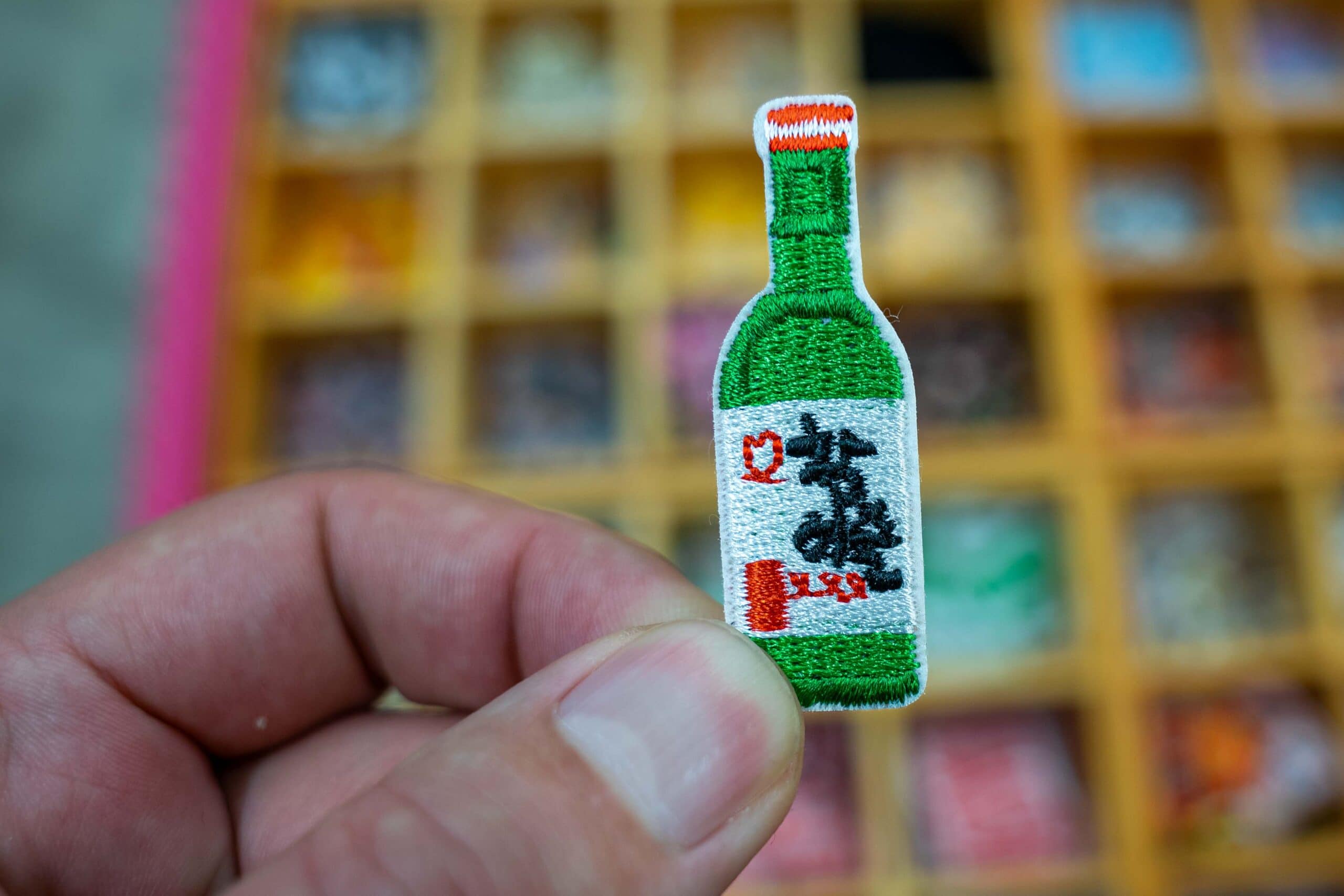 I'm holding a small patch you can sew onto clothing. This is a little green soju bottle, smaller than my thumb. It was for sale at a shop in Dongdaemun market