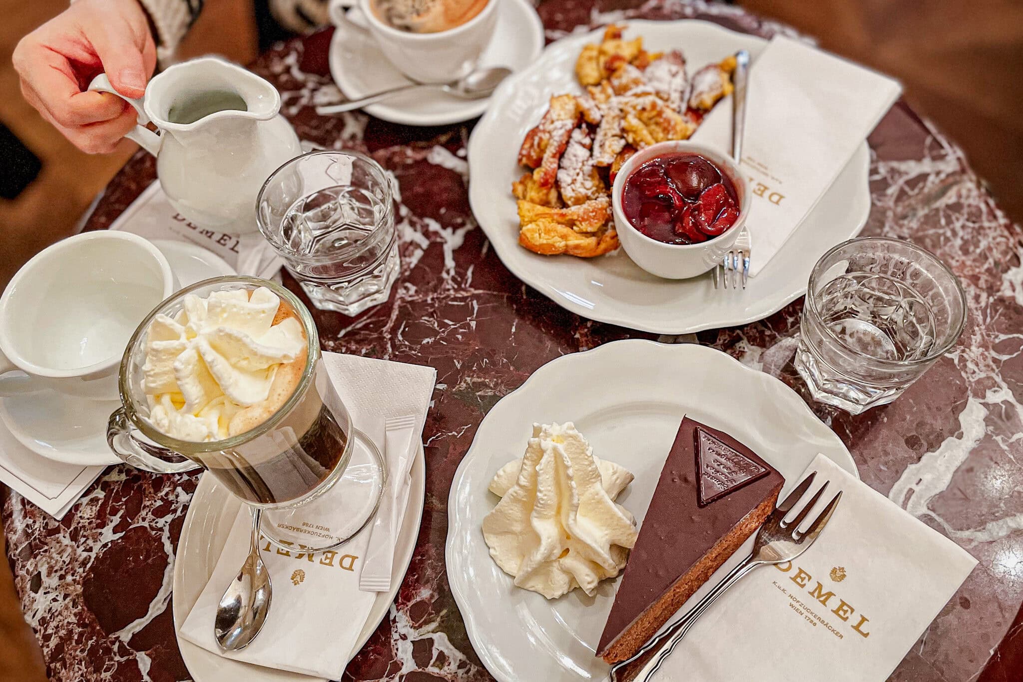 Our brunch at Cafe Demel: There is a fiaker coffee with whipped cream, a slice of Sachertorte, and a plate of Kaiserschmarrn with plum compote.