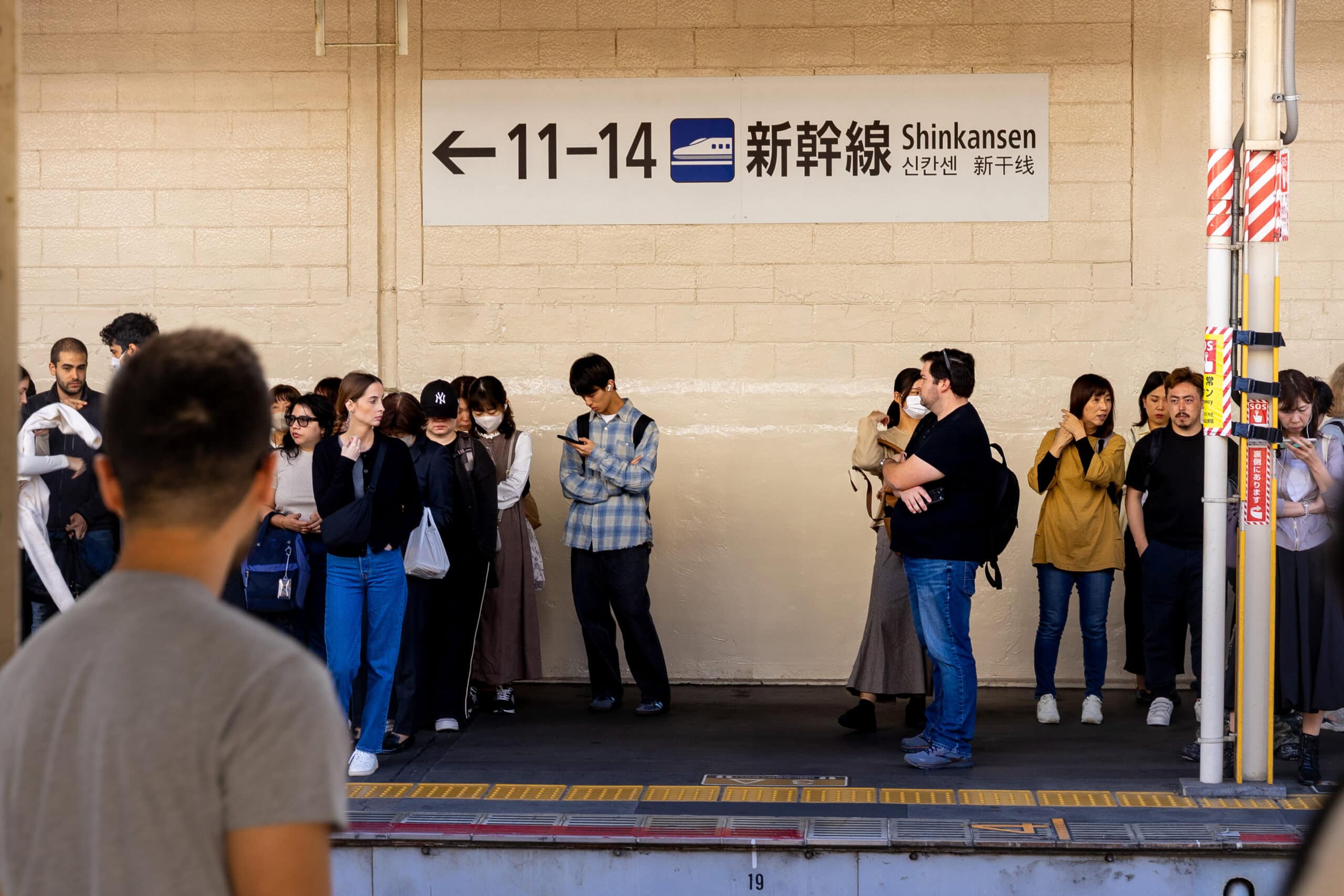 Passengers standing on the platform at Kyoto Station with a sign pointing to Shinkansen bullet trains