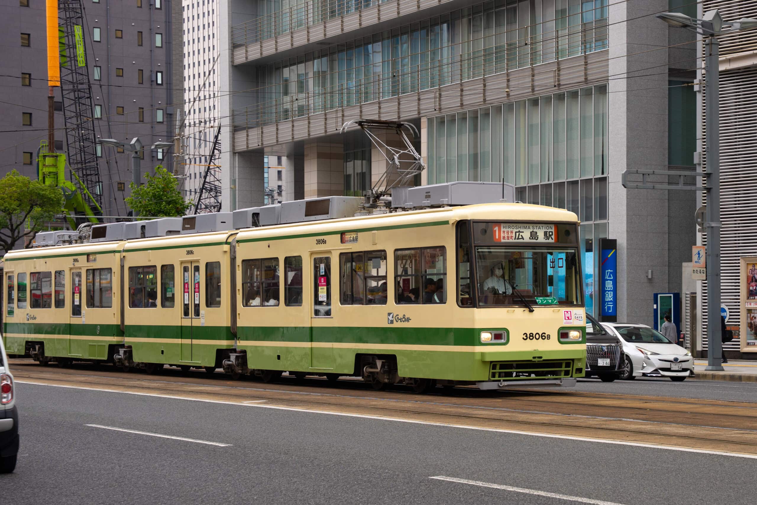 A green and beige tram on the streets of Hiroshima. It is tram number 1 and the destination is Hiroshima Station