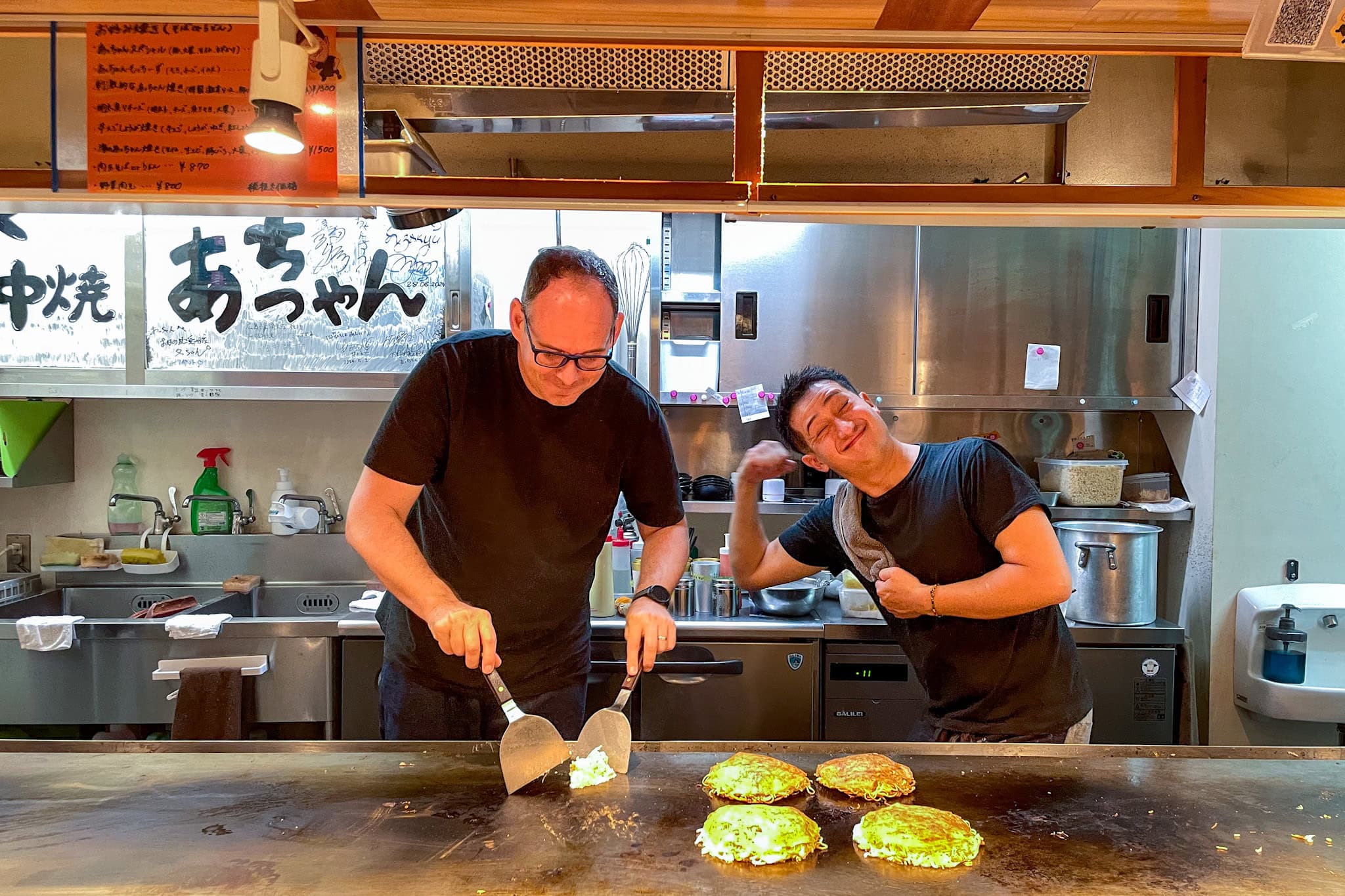 A photo of myself flipping a an okonomiyaki at Teppanyaki Acchan. The owner is joking around behind me