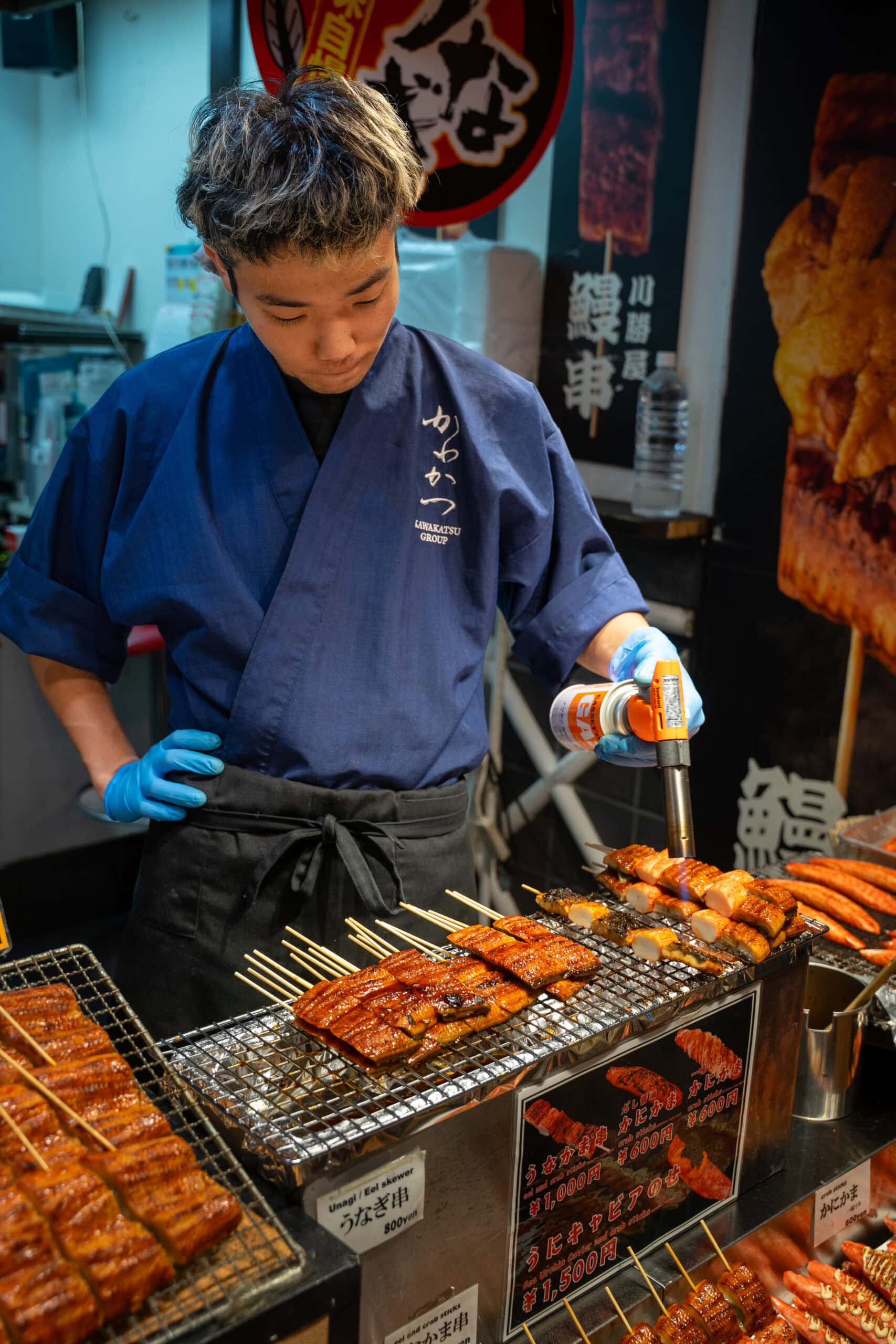 A young man uses a blow torch to grill eel in Nishiki food market, Kyoto
