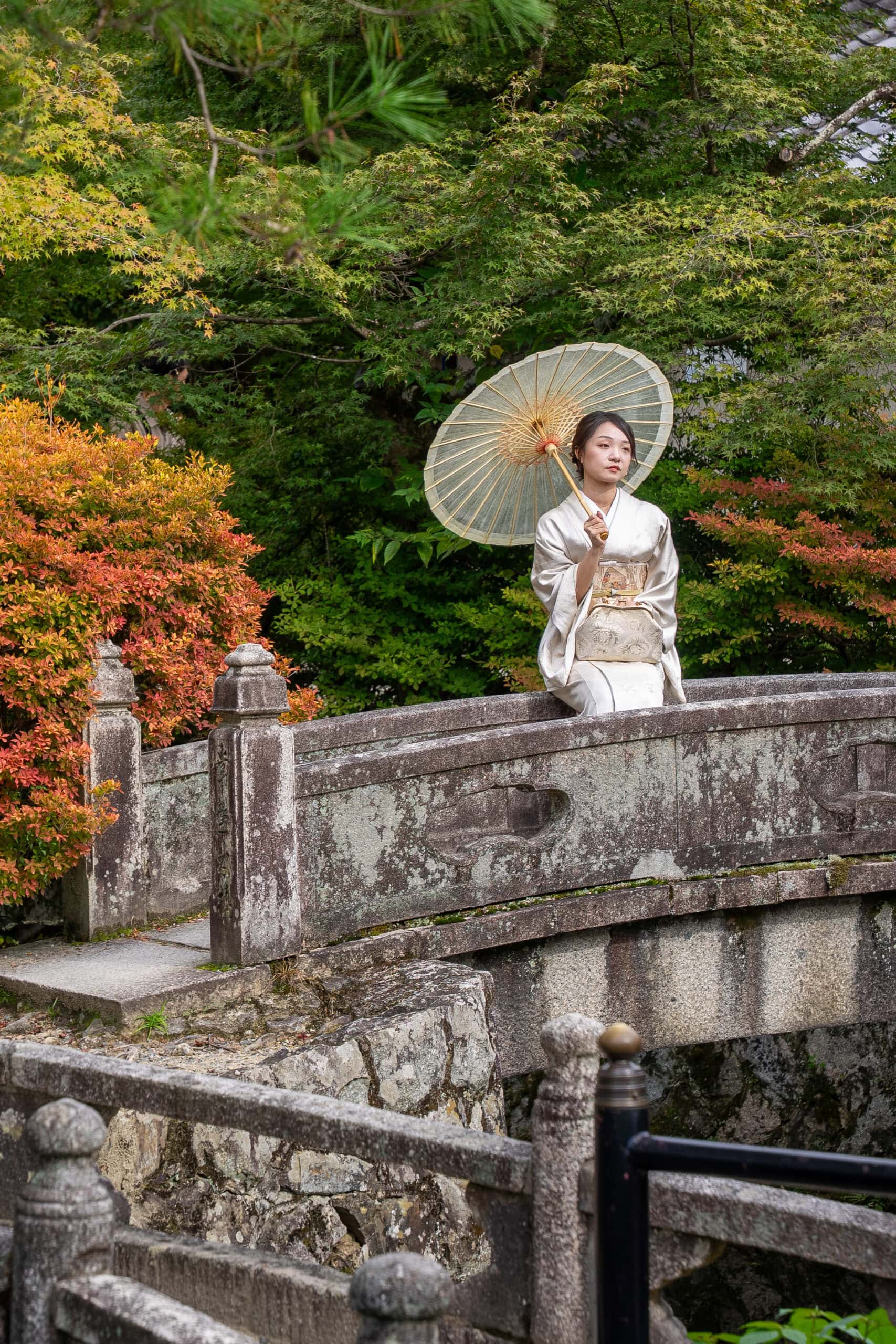 A woman in traditional Japanese dress with a paper umbrella poses for a phot at Kiyomizu-dera Temple