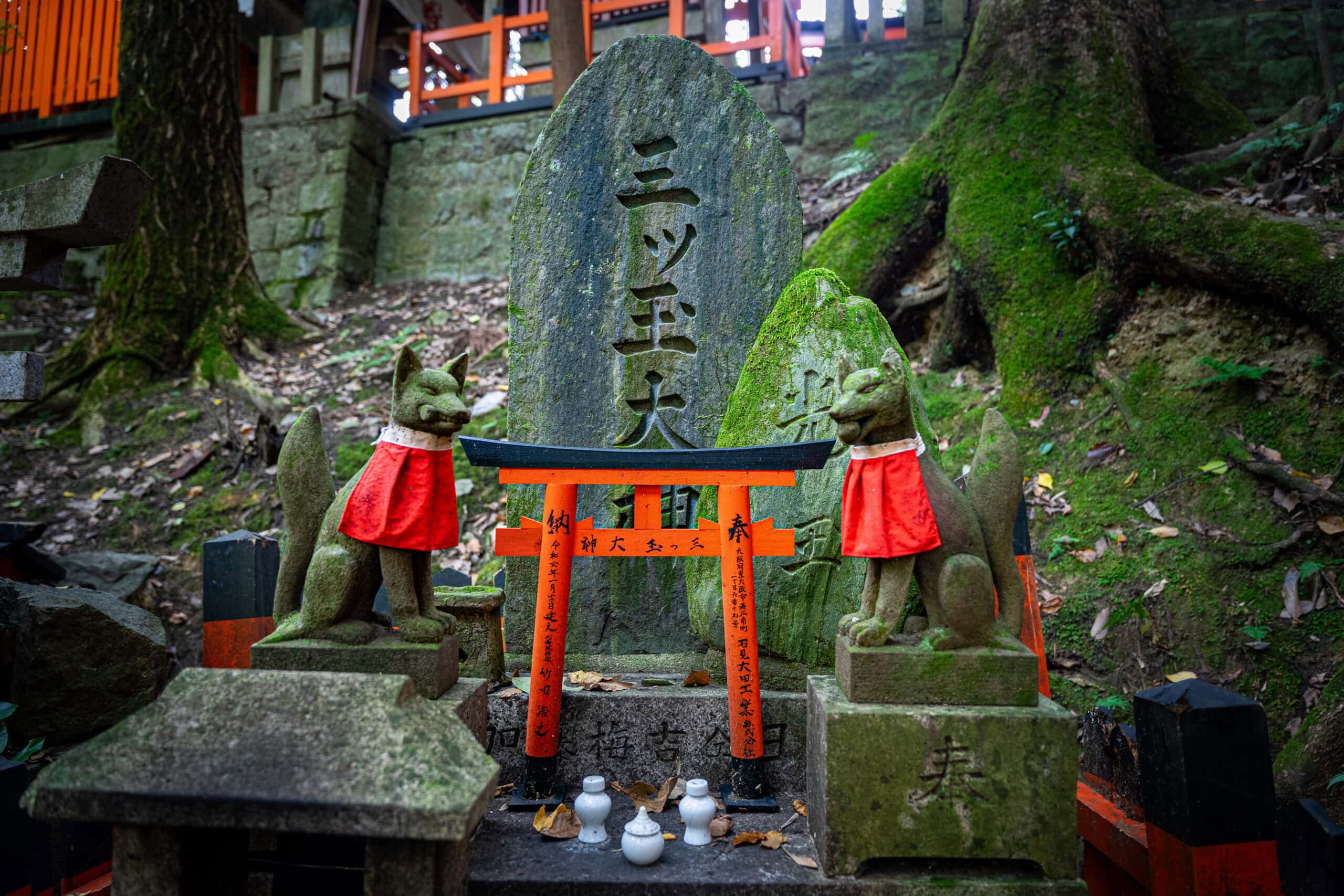 A small shrine with statues of two foxes, a small torii gate and three porcelain cups, seen at Fushimi Inari