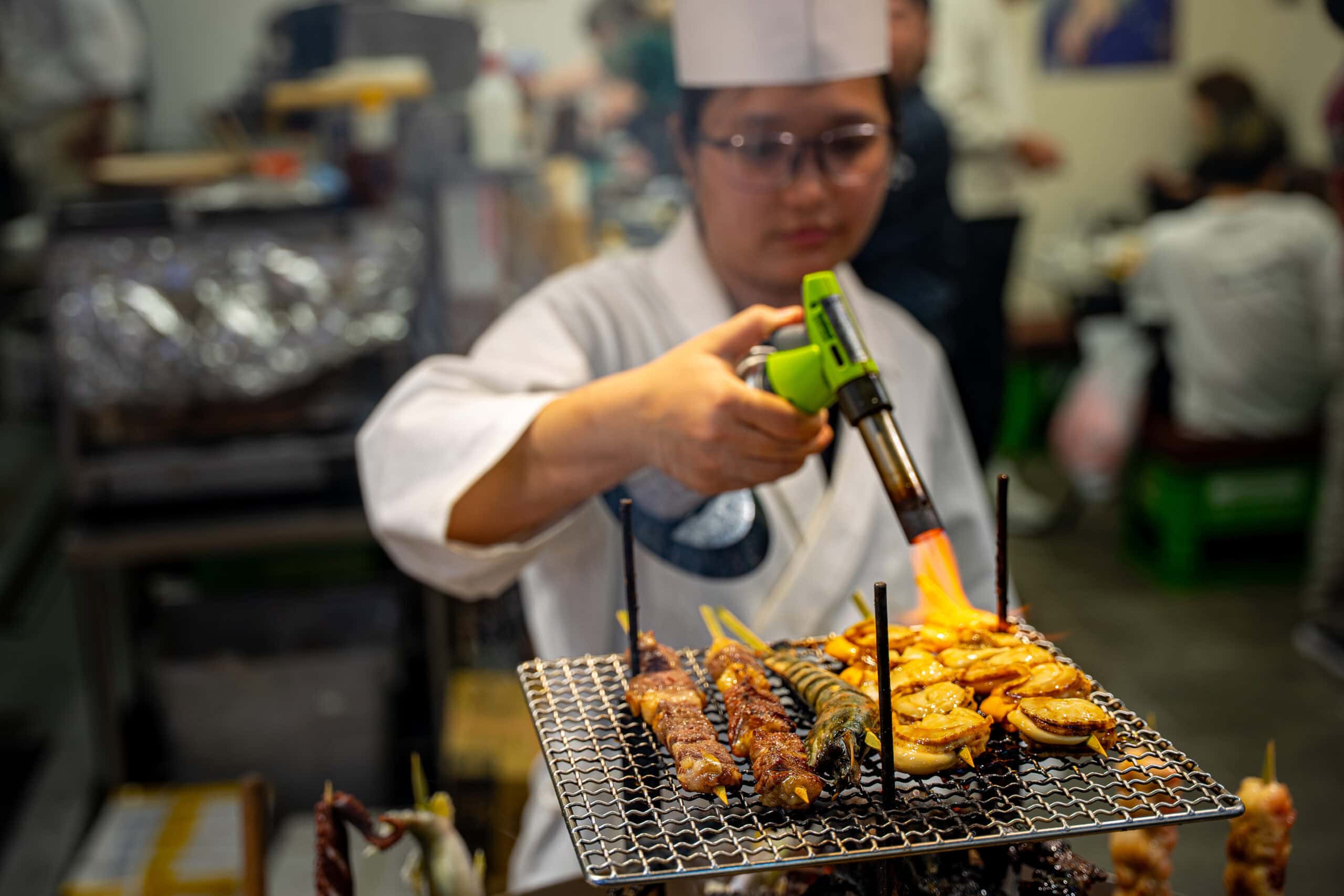A market vendor grill scallops, shrimp and meat skewers with a blow torch at Kurumon Market