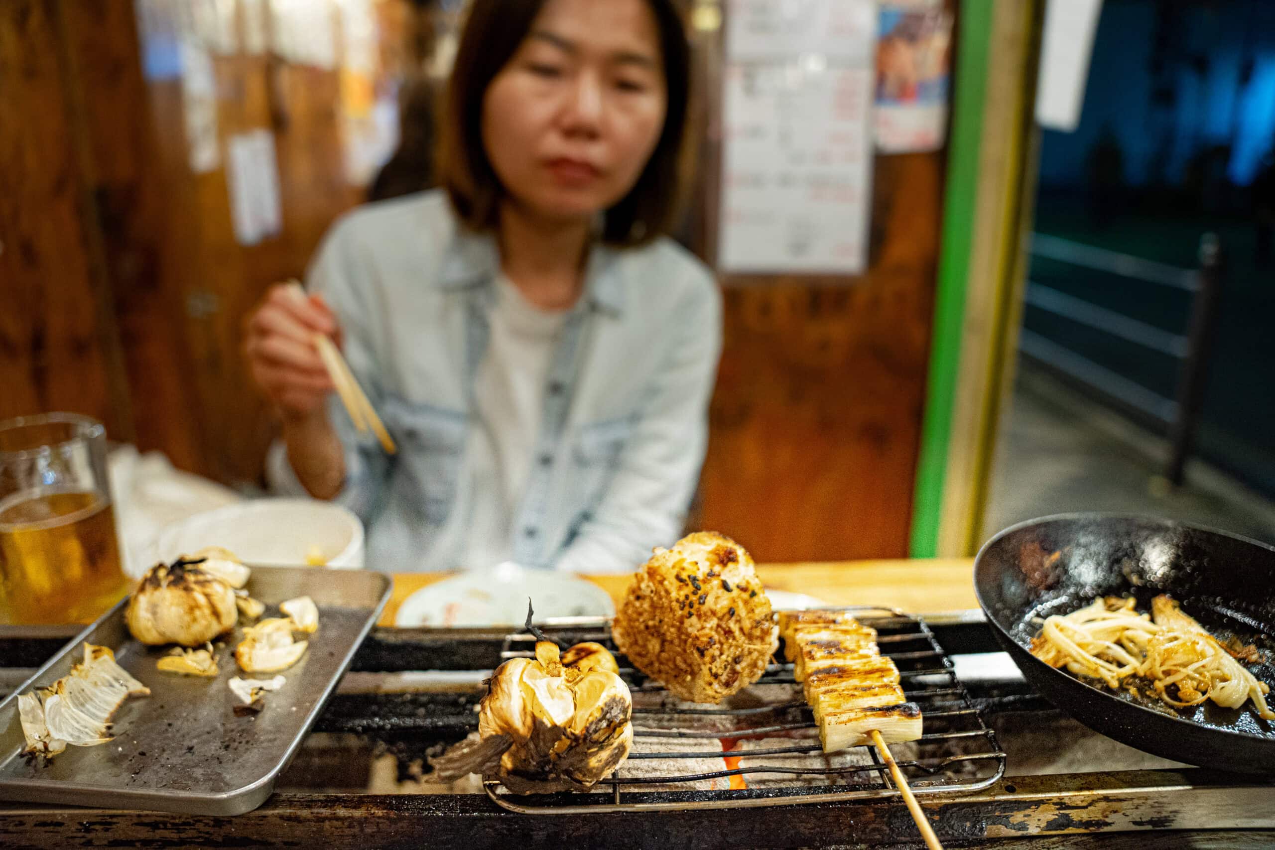 Jin grilling garlic, onigiri and leeks on the coals with chopsticks