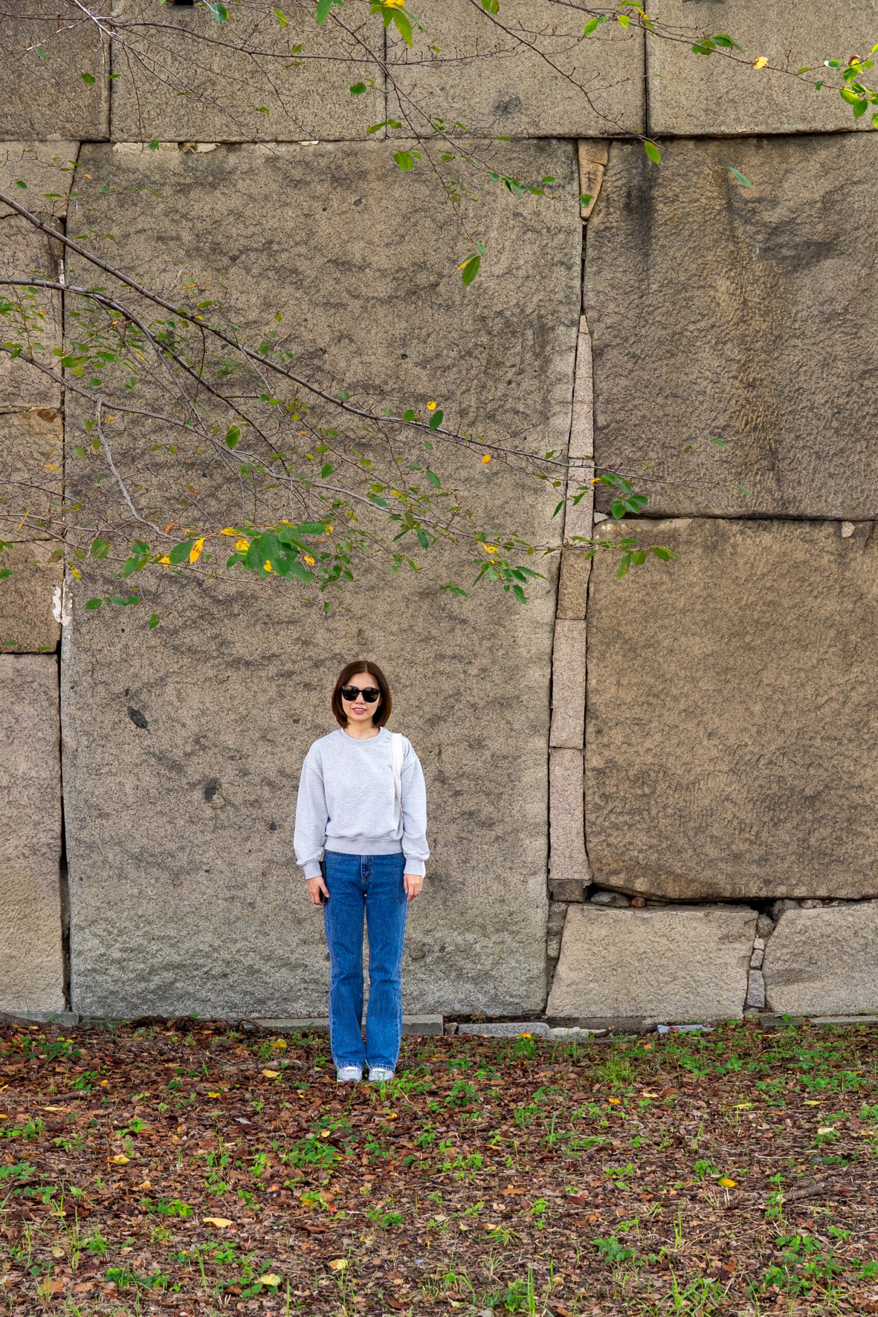 Jin stands in front of a large stone of the Osaka Castle wall. The stone is more than twice her height