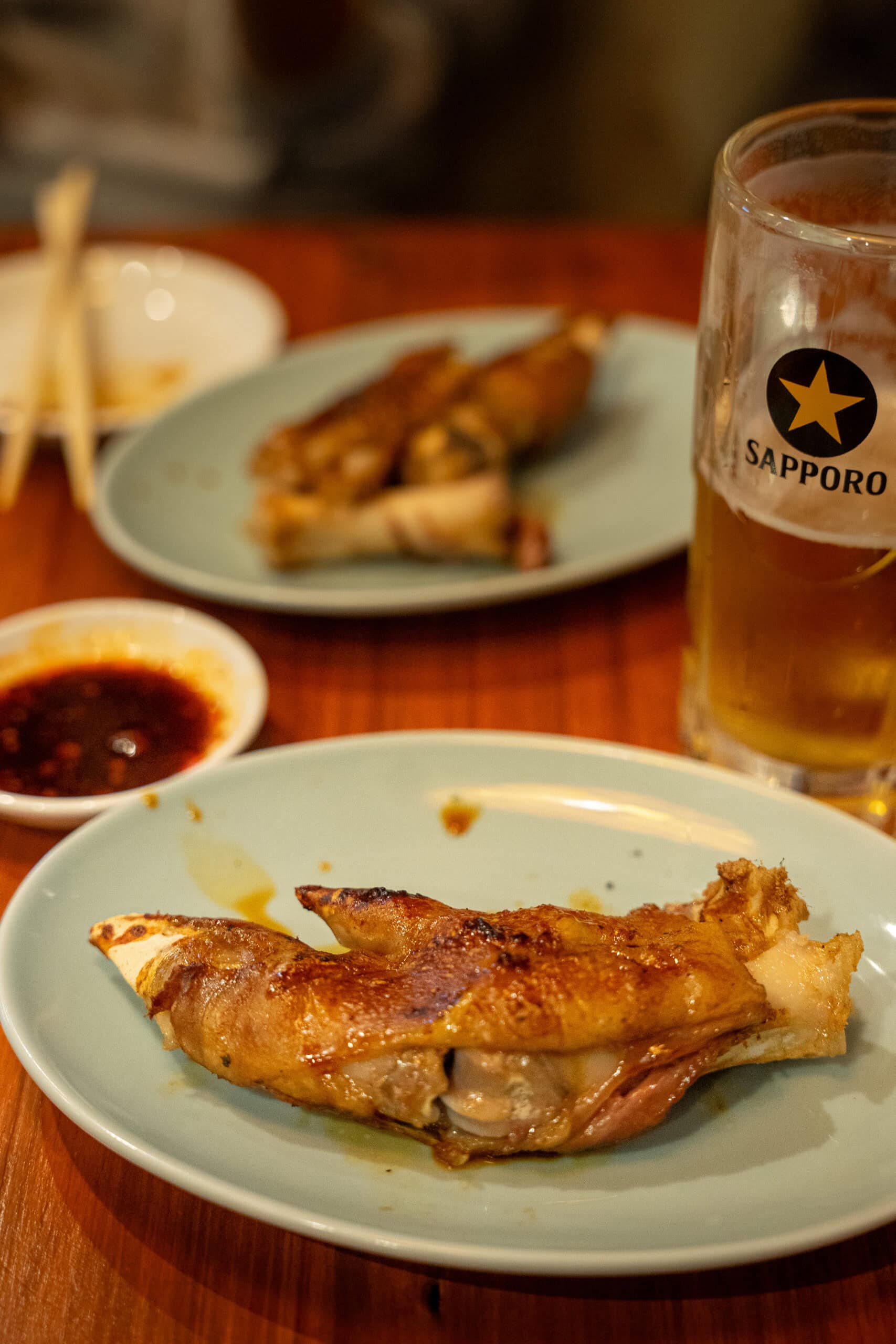 A plate with a grilled pork foot and a glass of Sapporo Lager