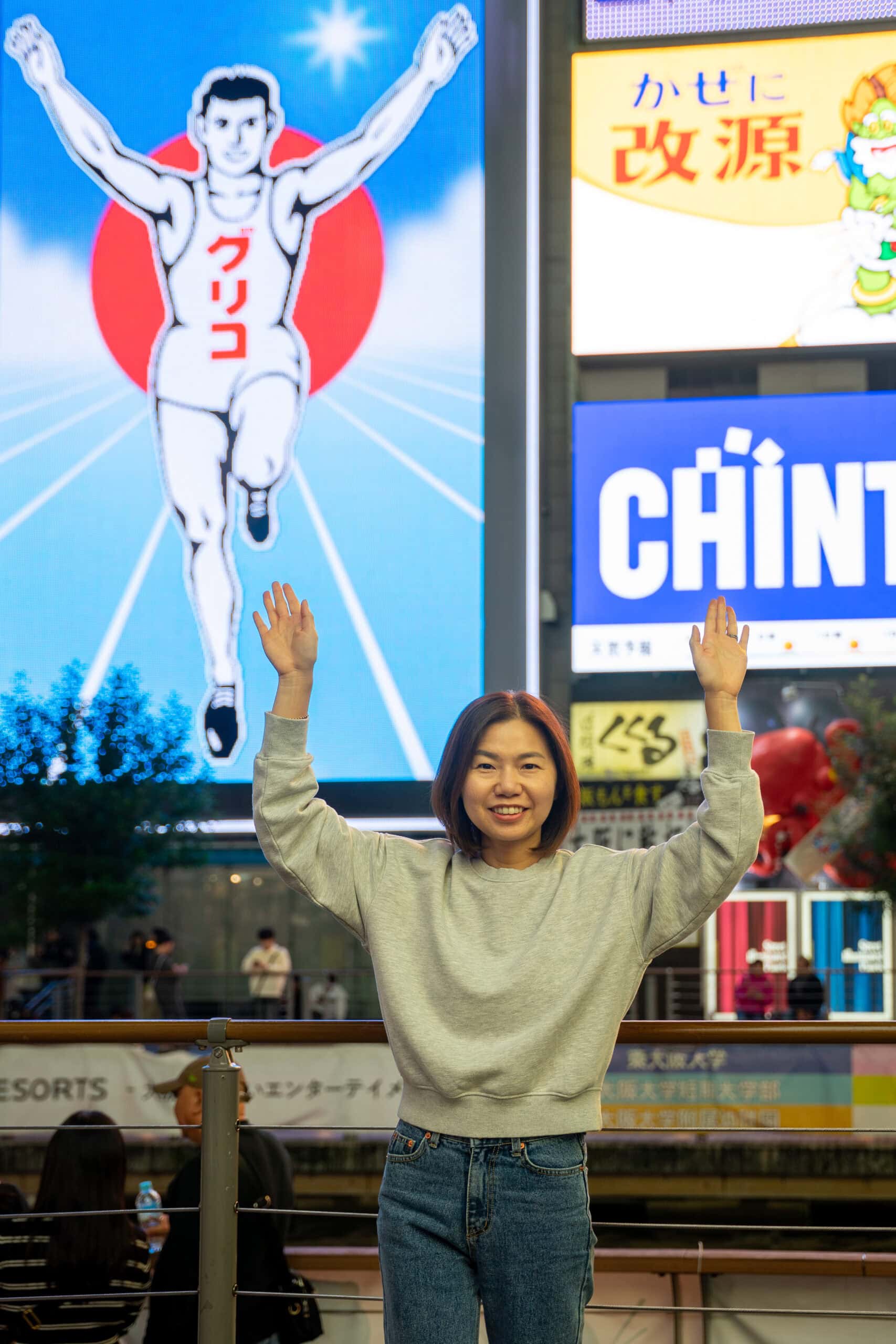 Jin poses with her hands in the air in front of the Glico man in Dotonburi