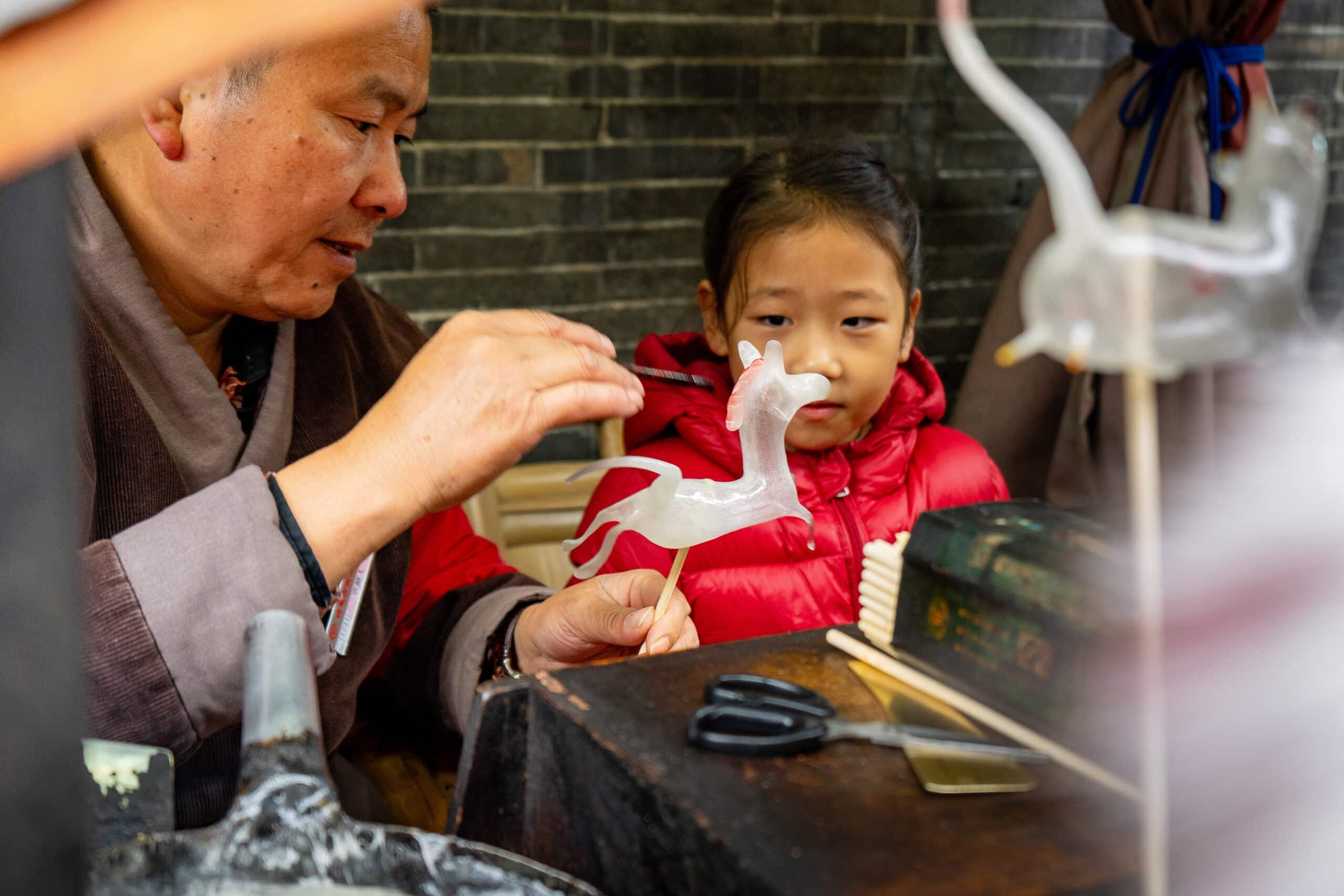 best-books-to-read-before-travelling-to-china: A man makes a horse figurine from sugar while a girls watches on in disbelief