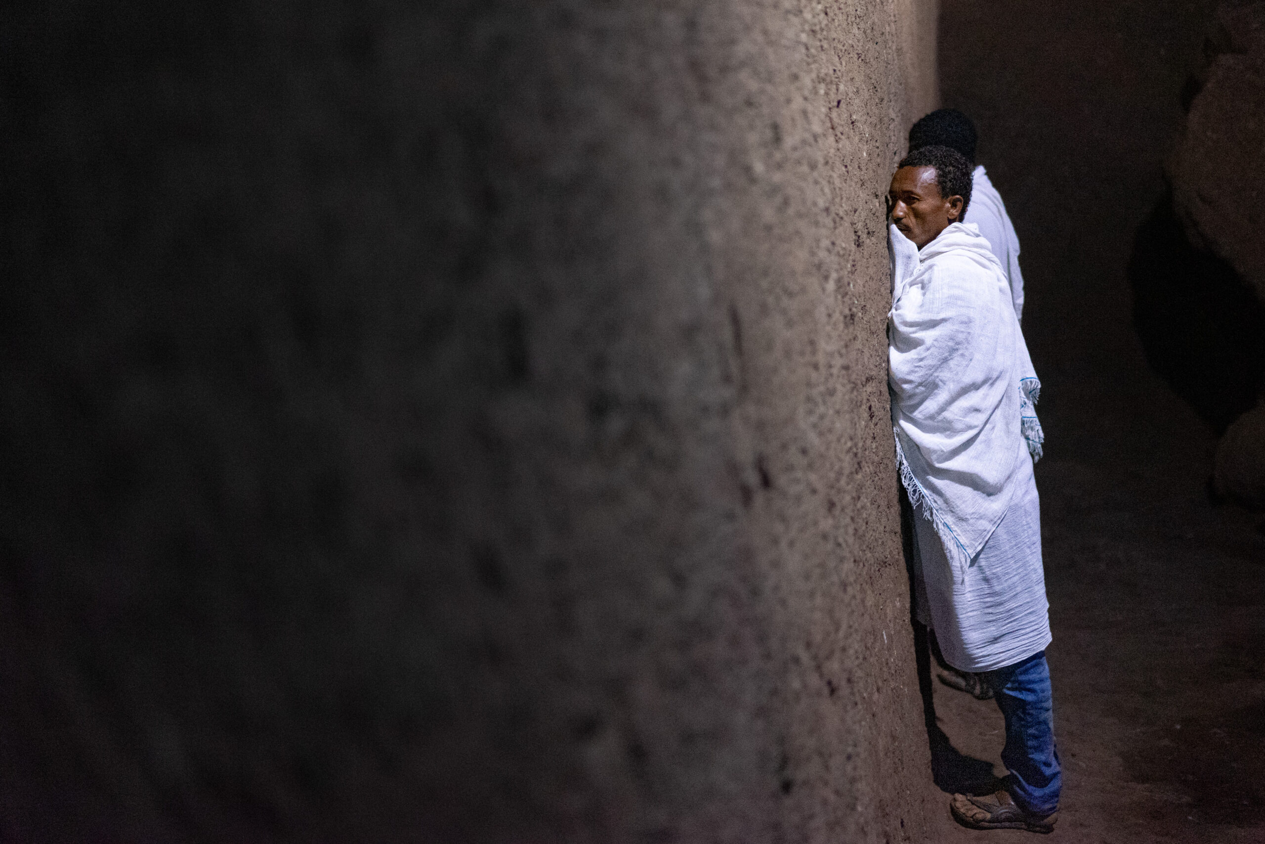 two men dressed in white shawls leans againts church walls as they pray during Sunday mass in the rock hewn church of Biet Medhane Alem
