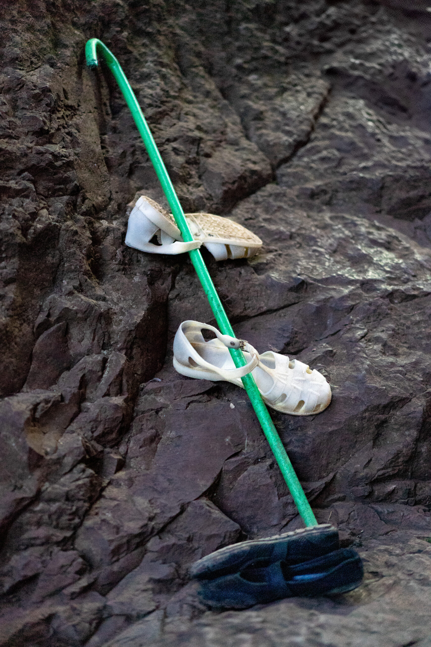 A close up of a green walking stick and white rubber sandals, balanced against rock, seen during Sunday mass in Lalibela