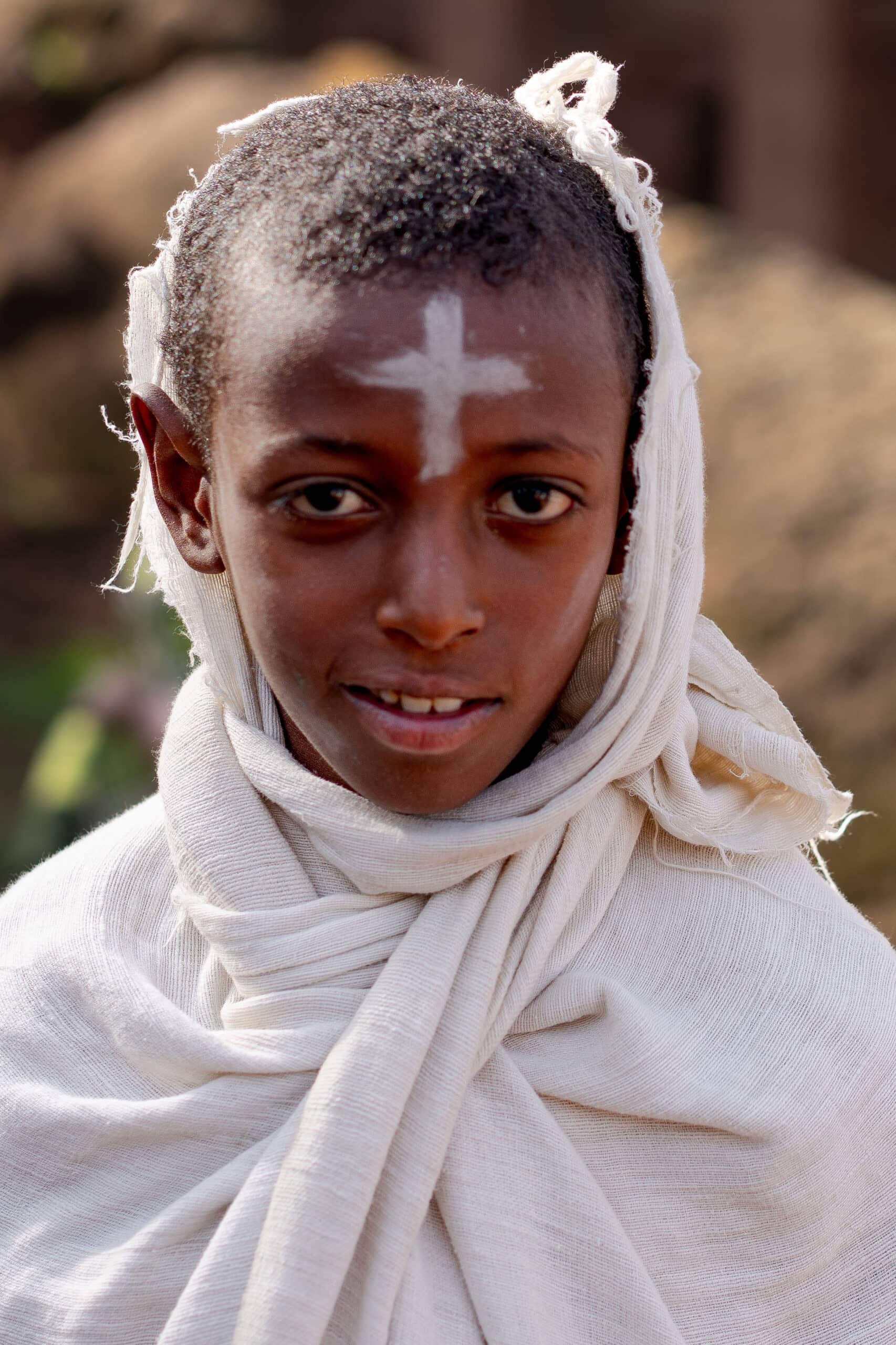 A youngEthiopian boy with a white cross painted on his face, seen on a Sunday morning in Lalibela